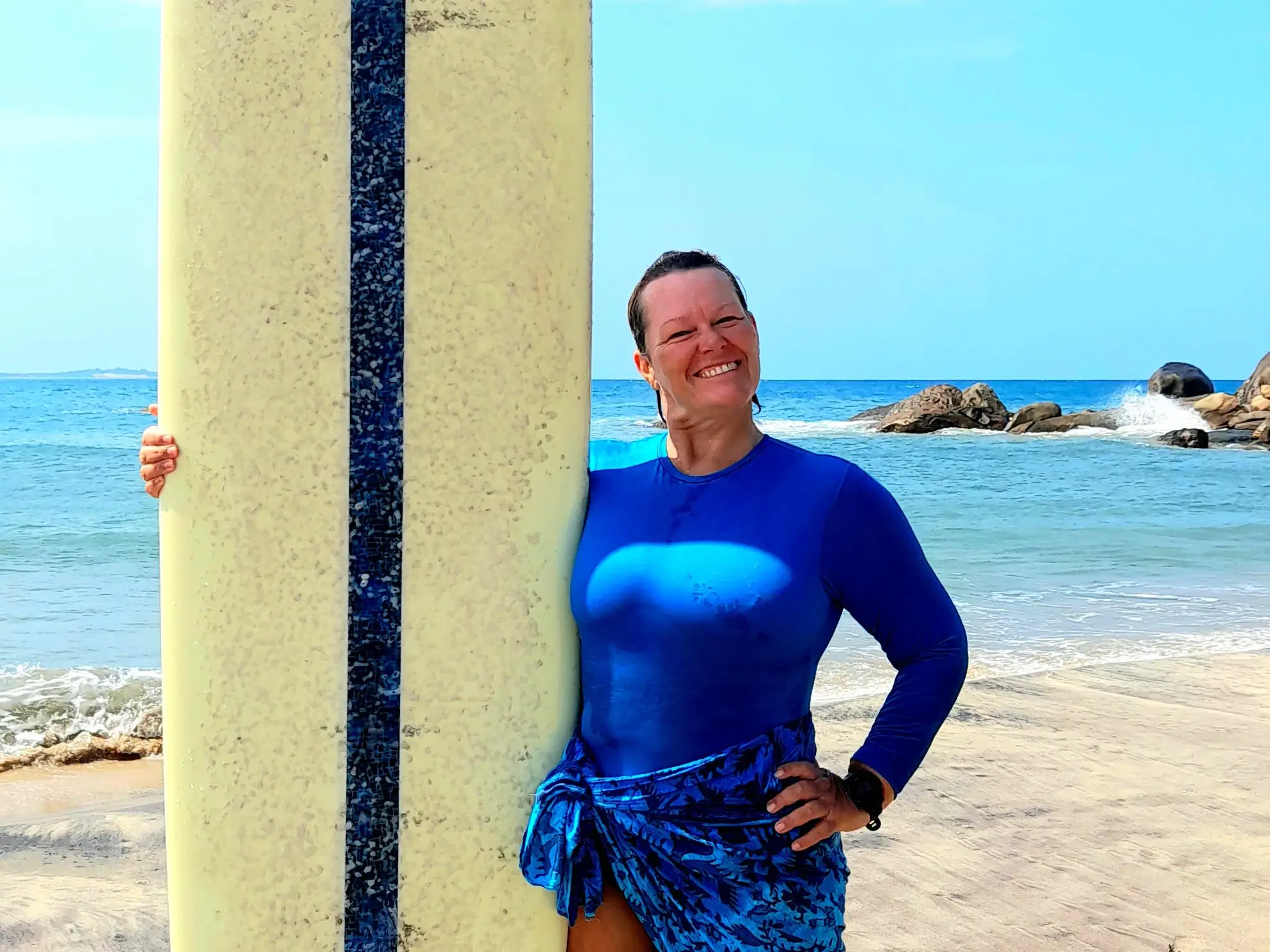 A woman posing with her surfboard on the beach.