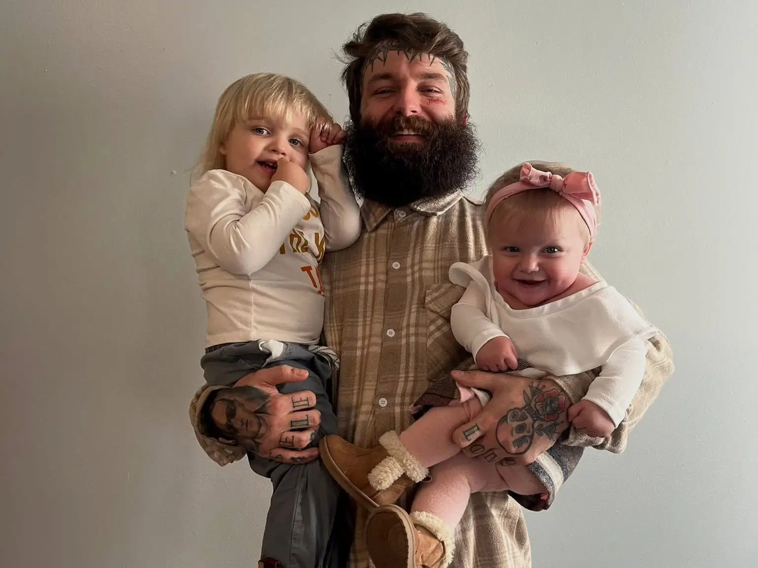A bearded father holding two young children in his arms.
