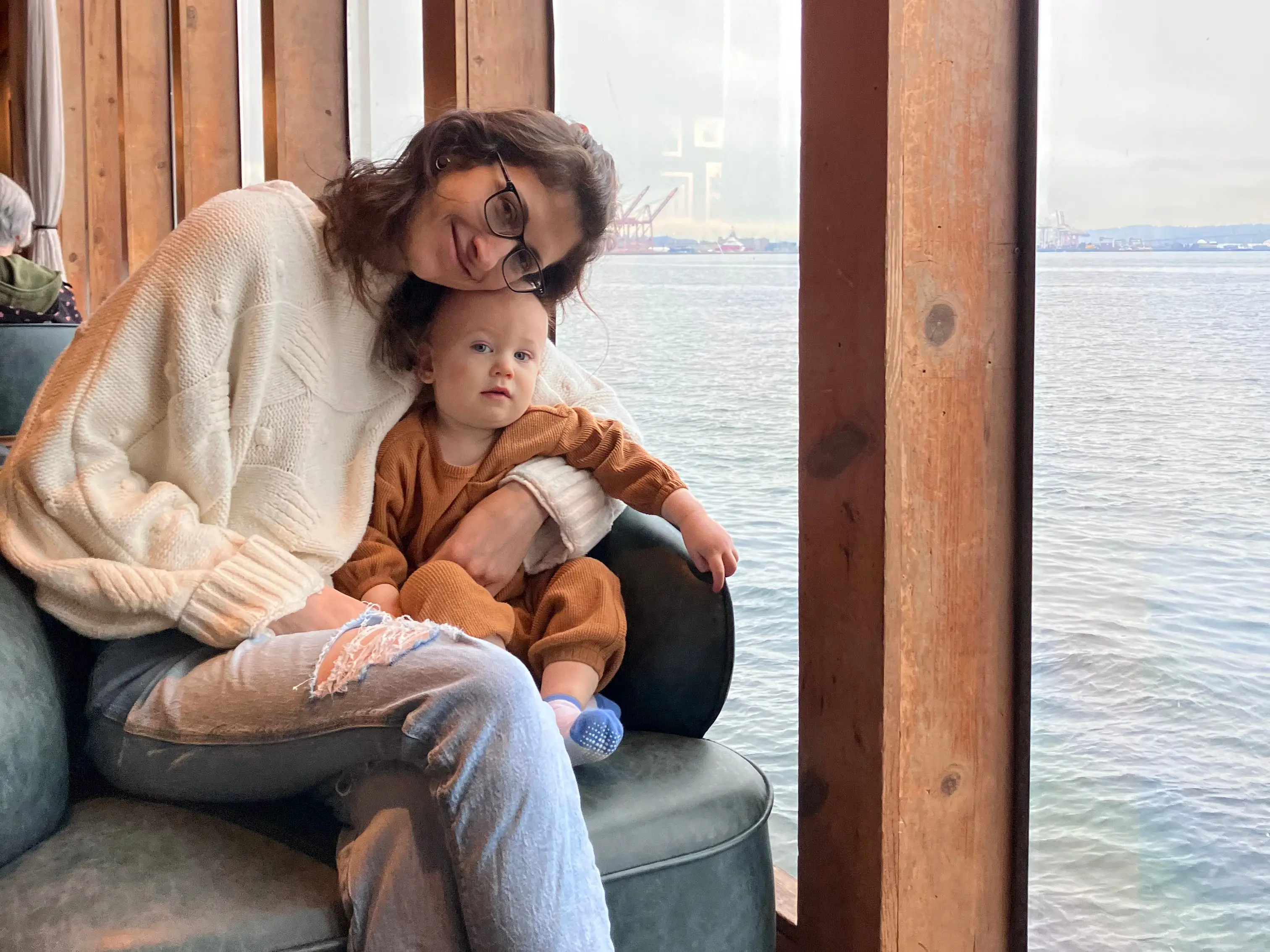 Woman smiling in chair with baby next to window with ocean views