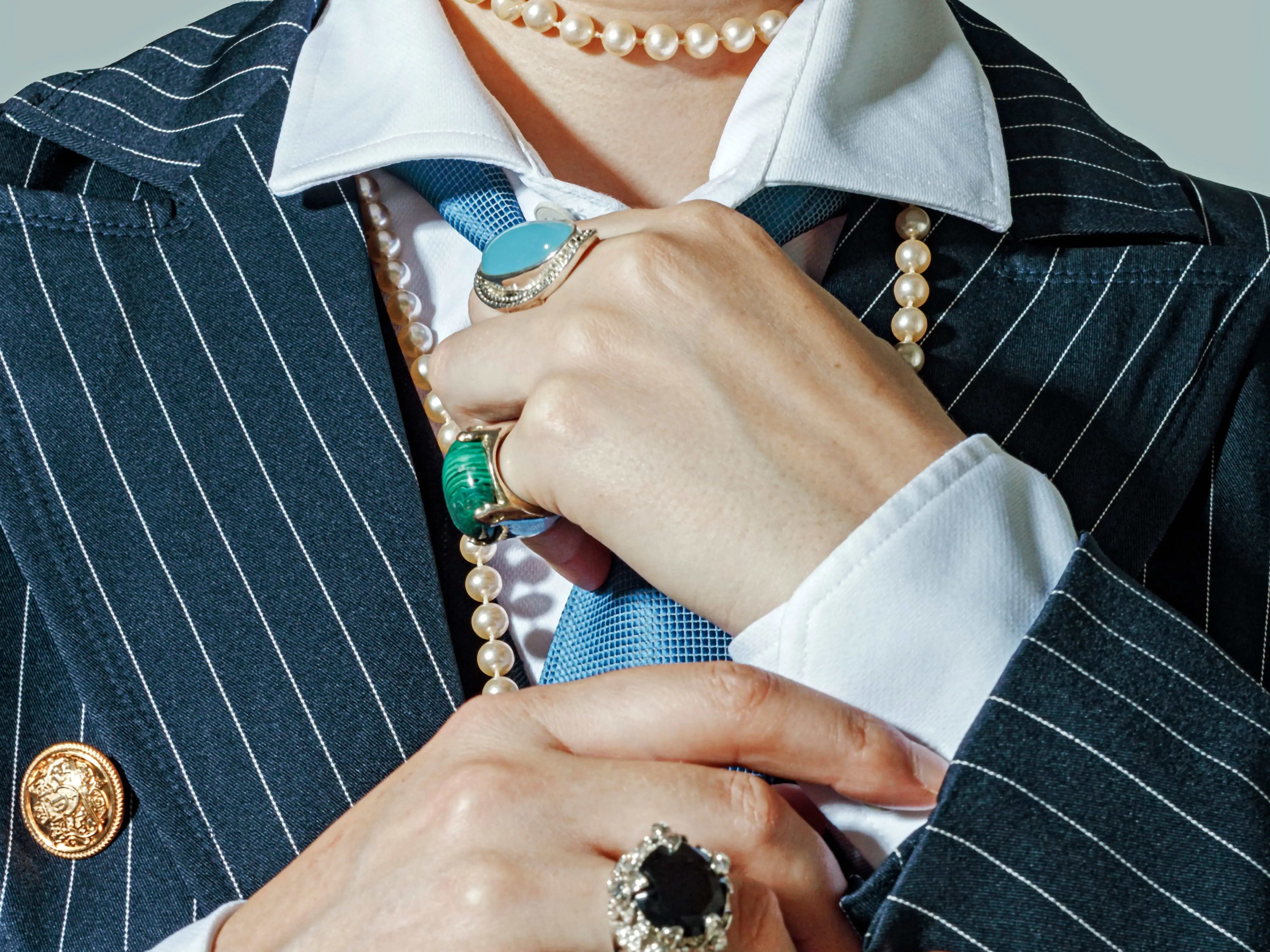 A well-dressed woman wearing a pearl necklace and vintage-looking rings.
