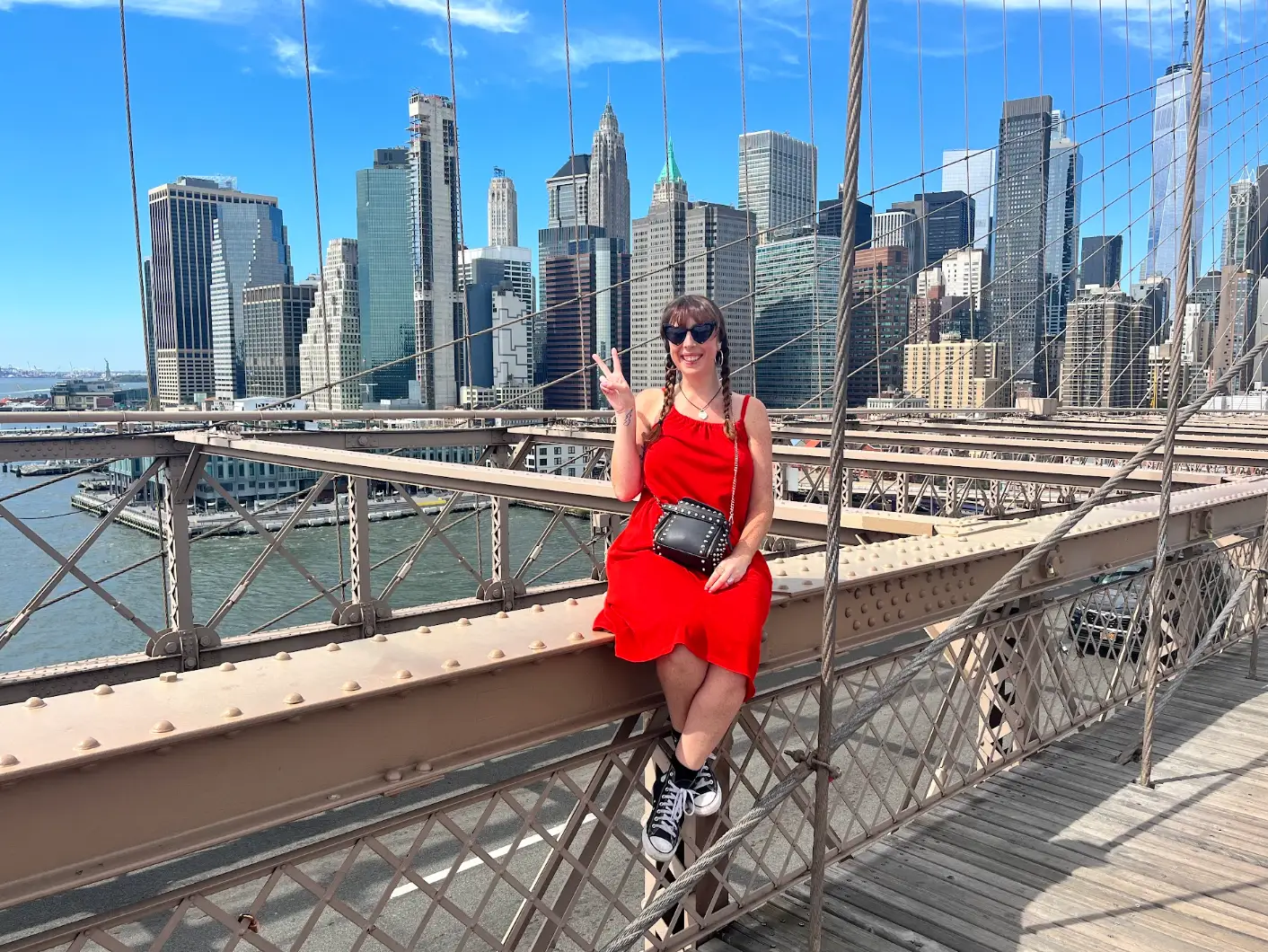 The writer wearing a red dress and sitting on a bridge in New York City, with skyscrapers in the background.