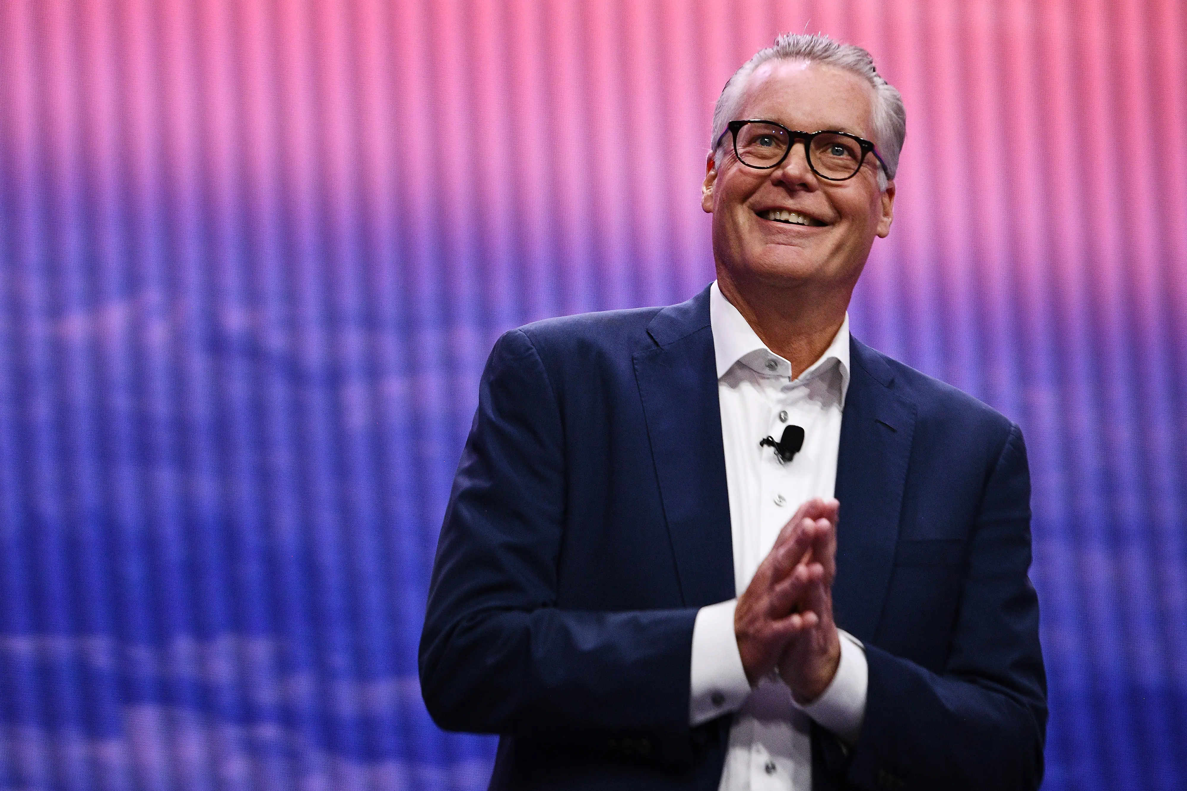 Ed Bastian stands in front of a pink and blue wall. He hands are pressed together.