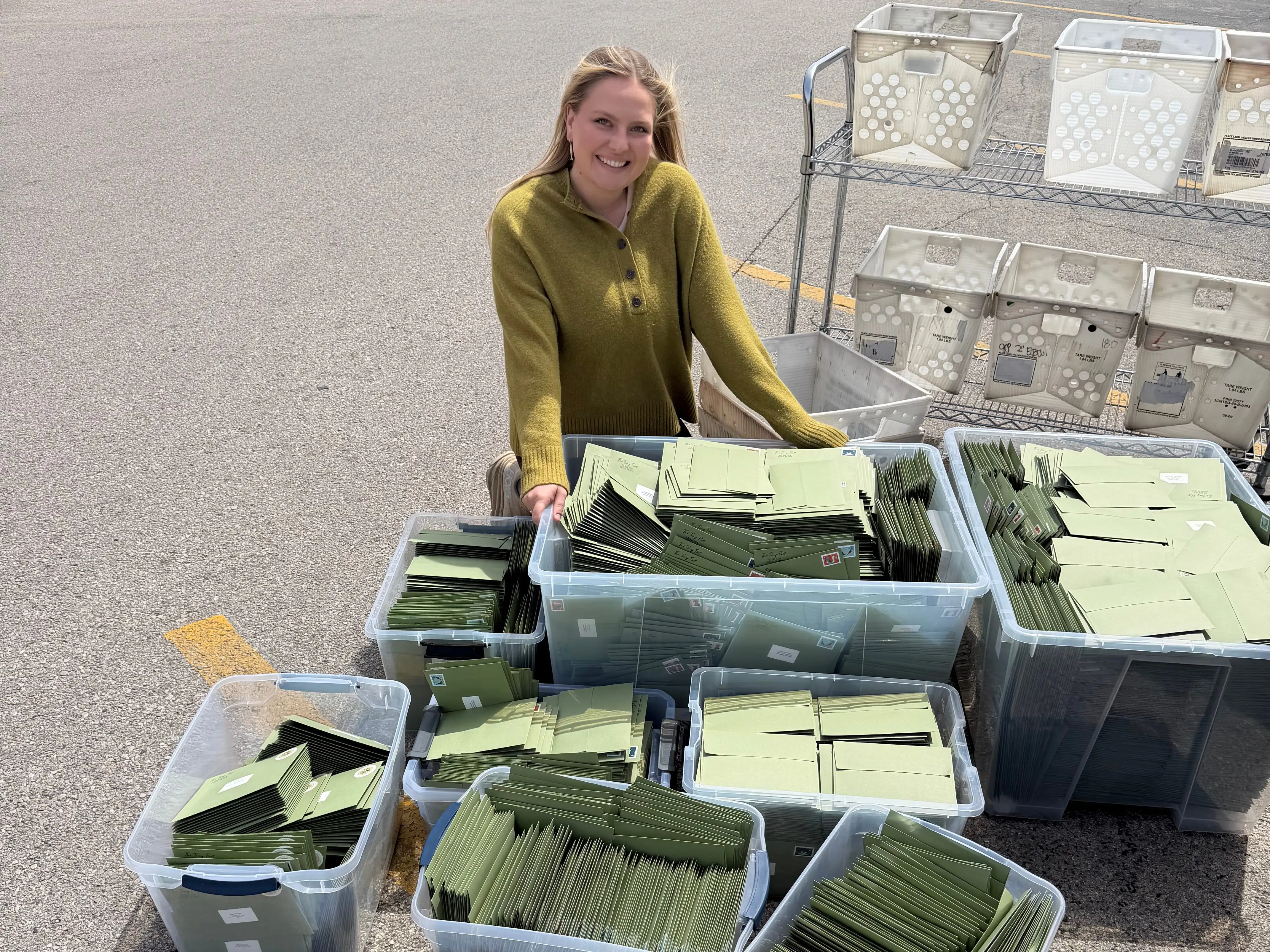 A woman with eight boxes filled with green envelopes.