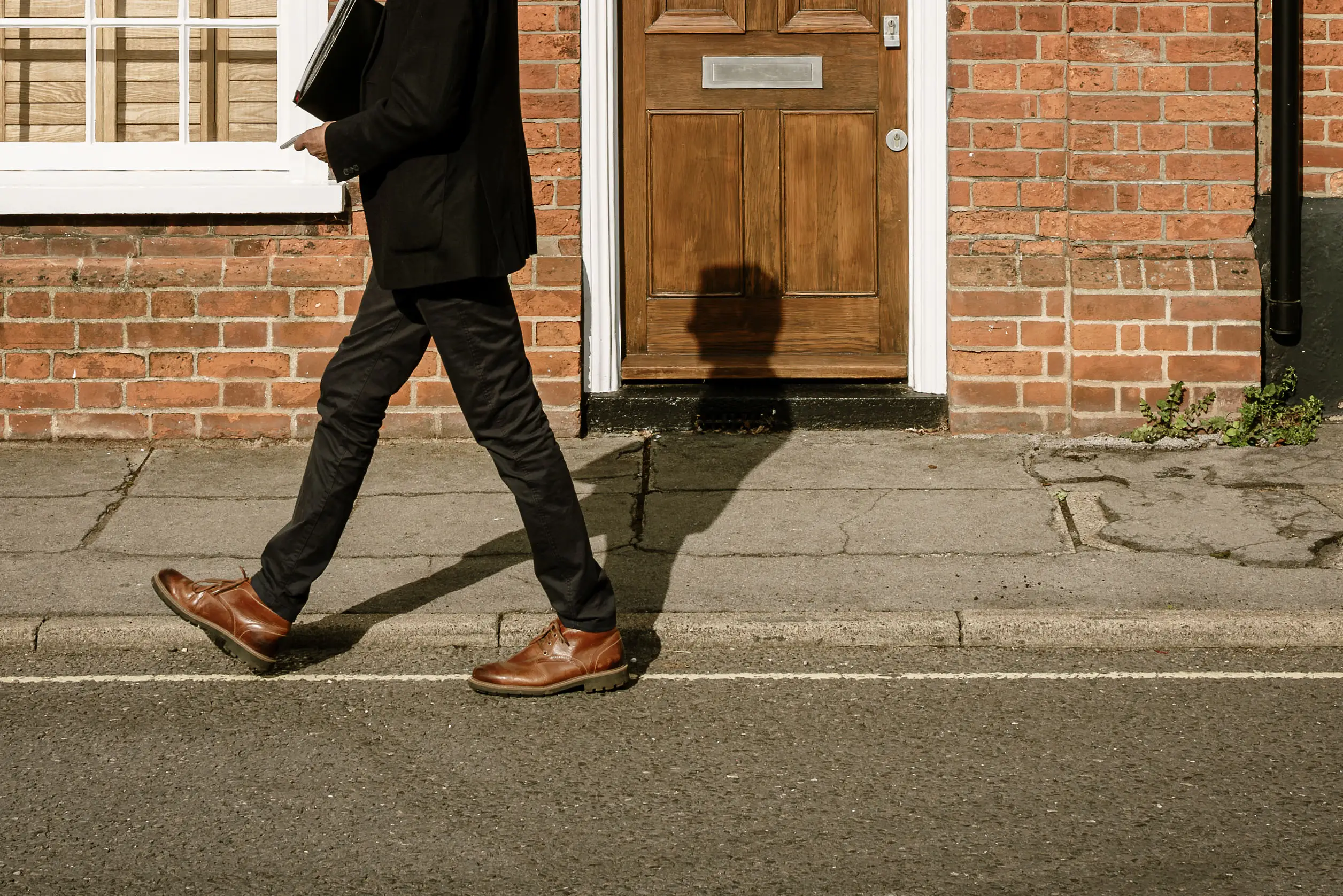 Abstract view of a male Estate Agent seen walking down a terraced English street. The shadow of the mans head creates an abstract appearance to his body.