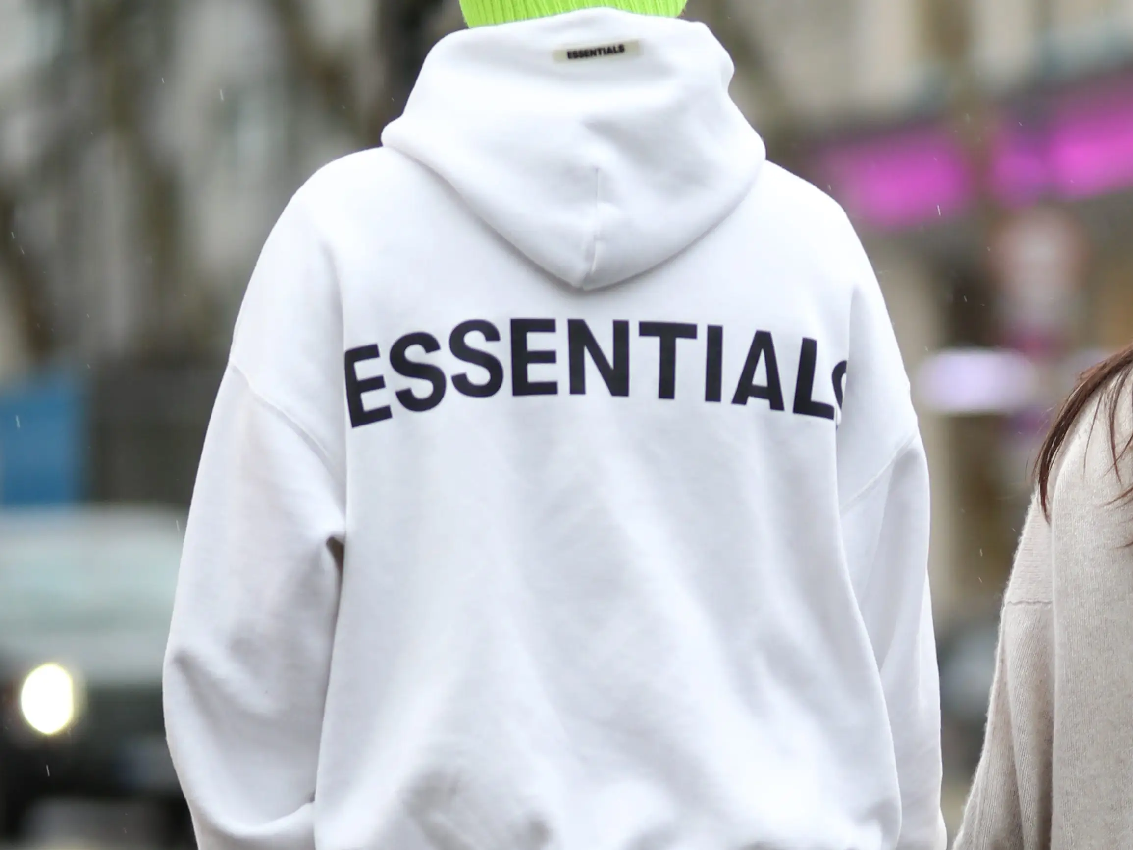 A man wears a Fear of God Essentials hoodie.