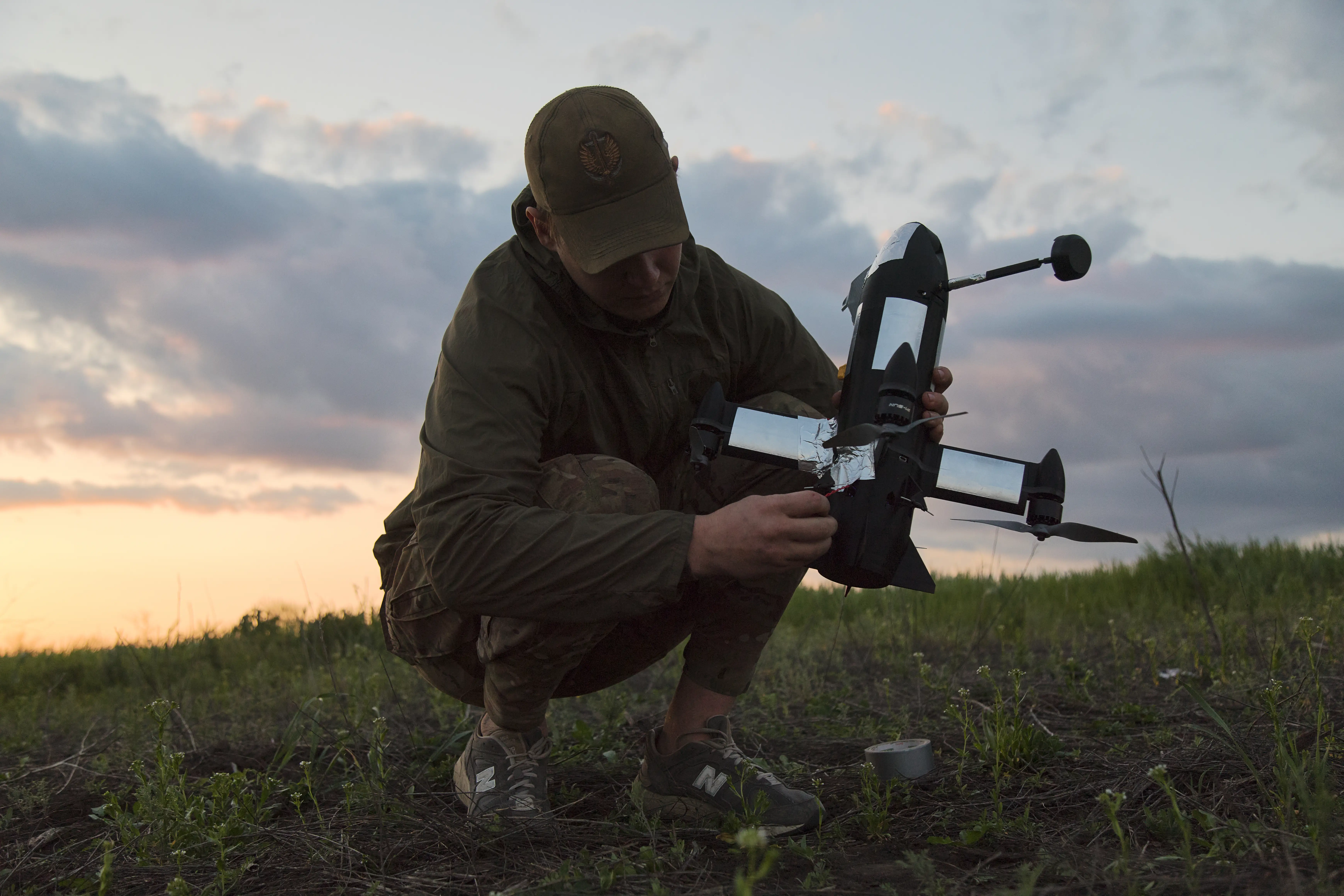 A Ukrainian man crouches as he holds a P1-Sun interceptor drone and prepares it for launch.