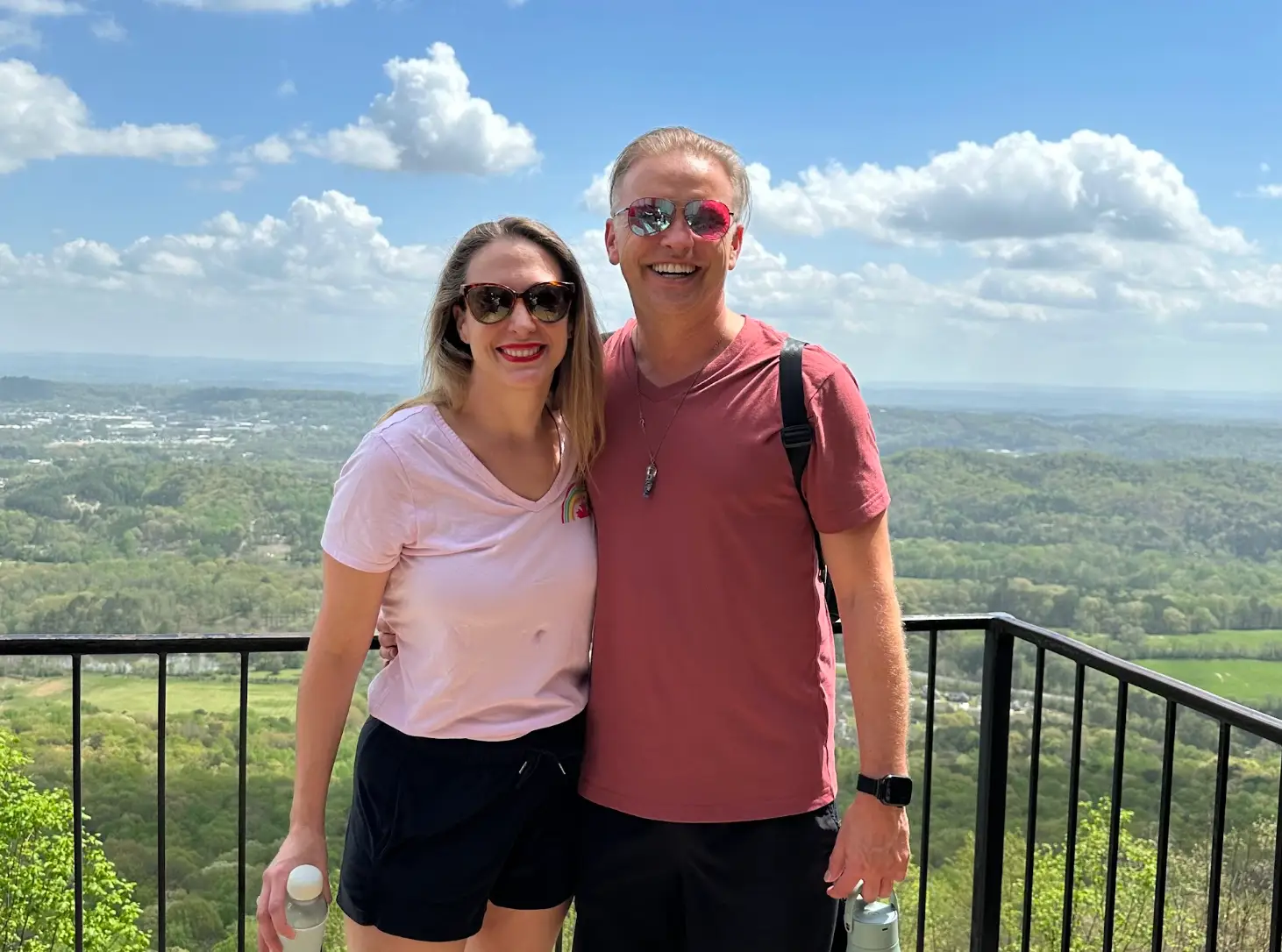 The writer and her partner standing on a balcony overlooking greenery and clouds.