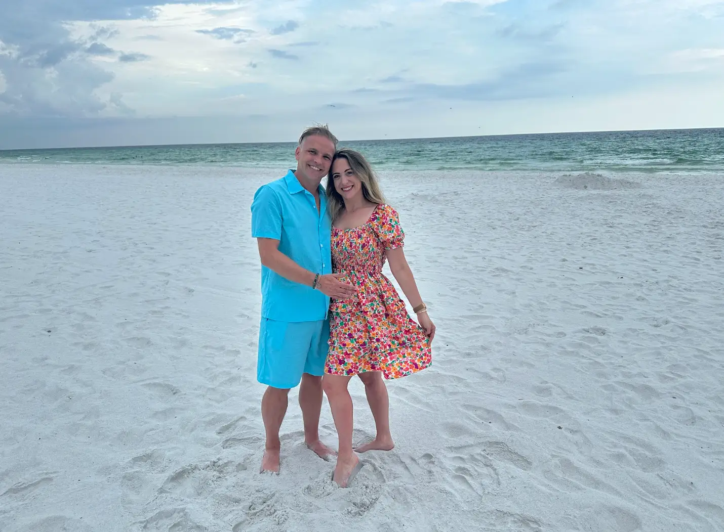 The writer wearing a dress and standing next to her husband on an empty beach.