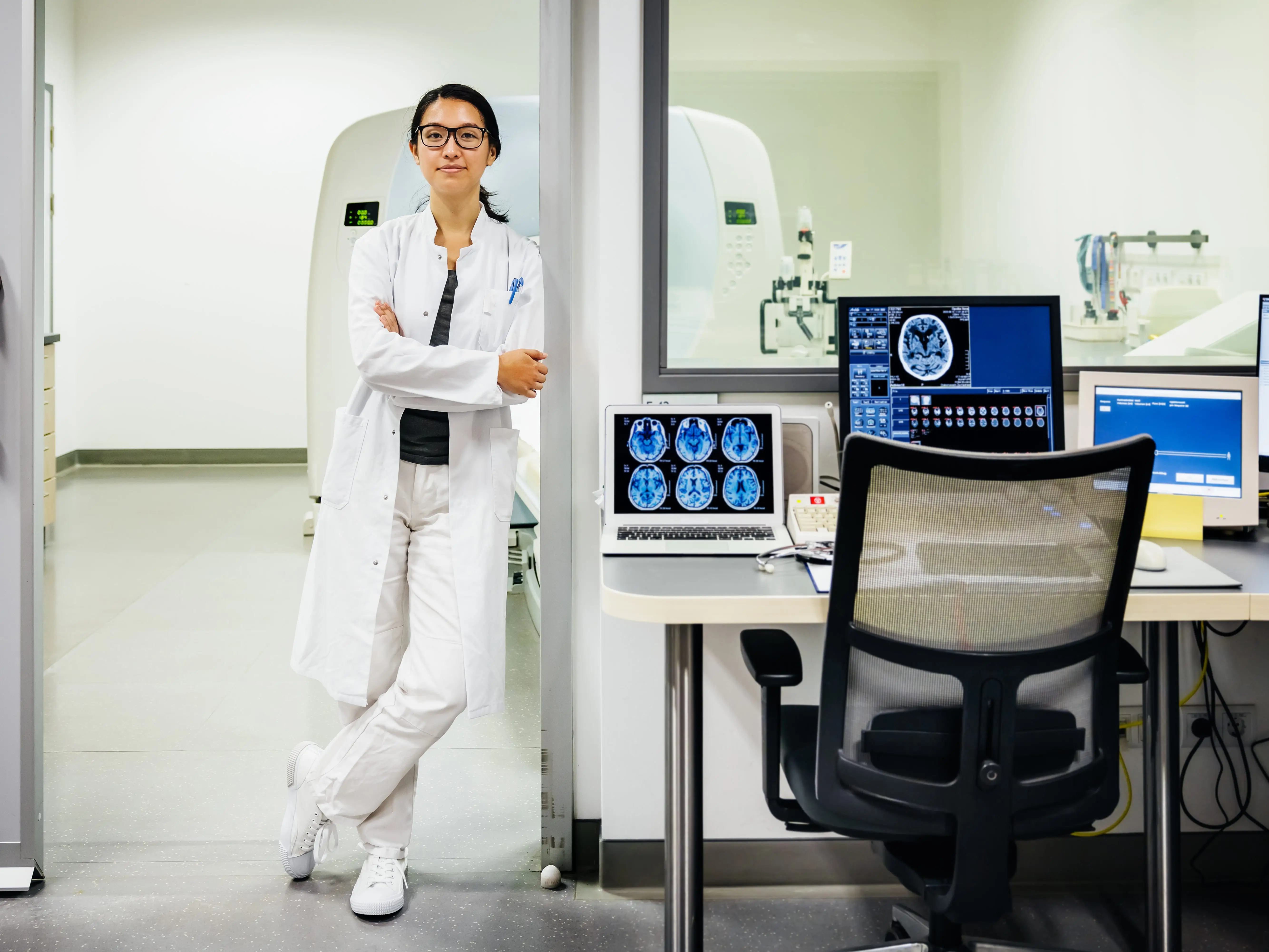 A radiologist standing with her arms crossed next to MRI control screens