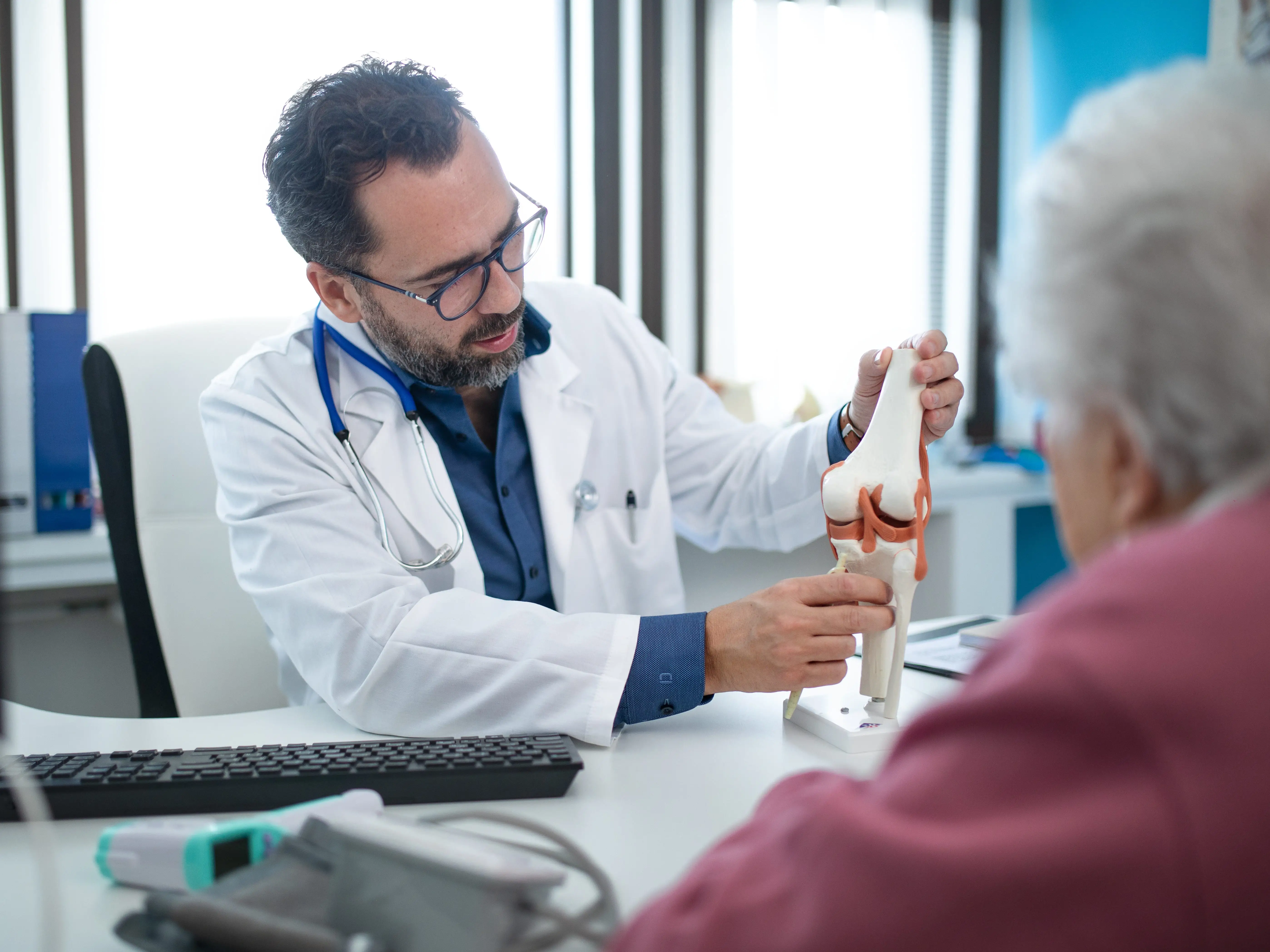 An orthopedic doctor holding an artificial joint and showing it to a patient