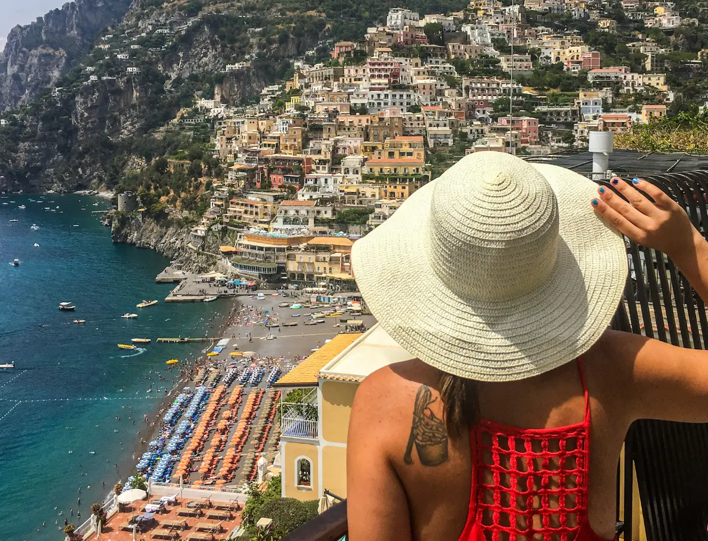The writer wearing a sunhat and gazing out at buildings and the water in Positano, Italy.