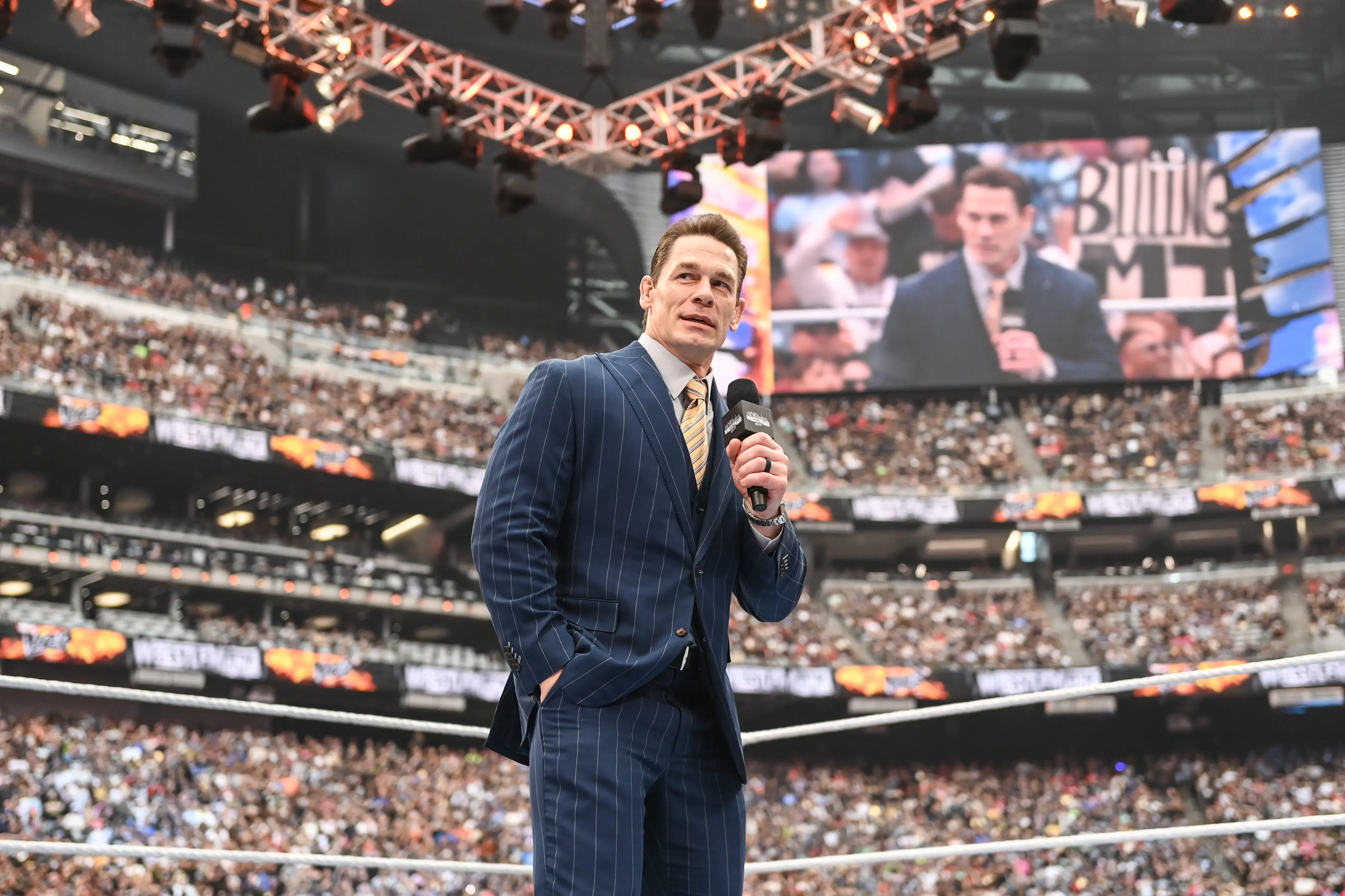 John Cena stands in the ring as an announcer at a packed WWE event