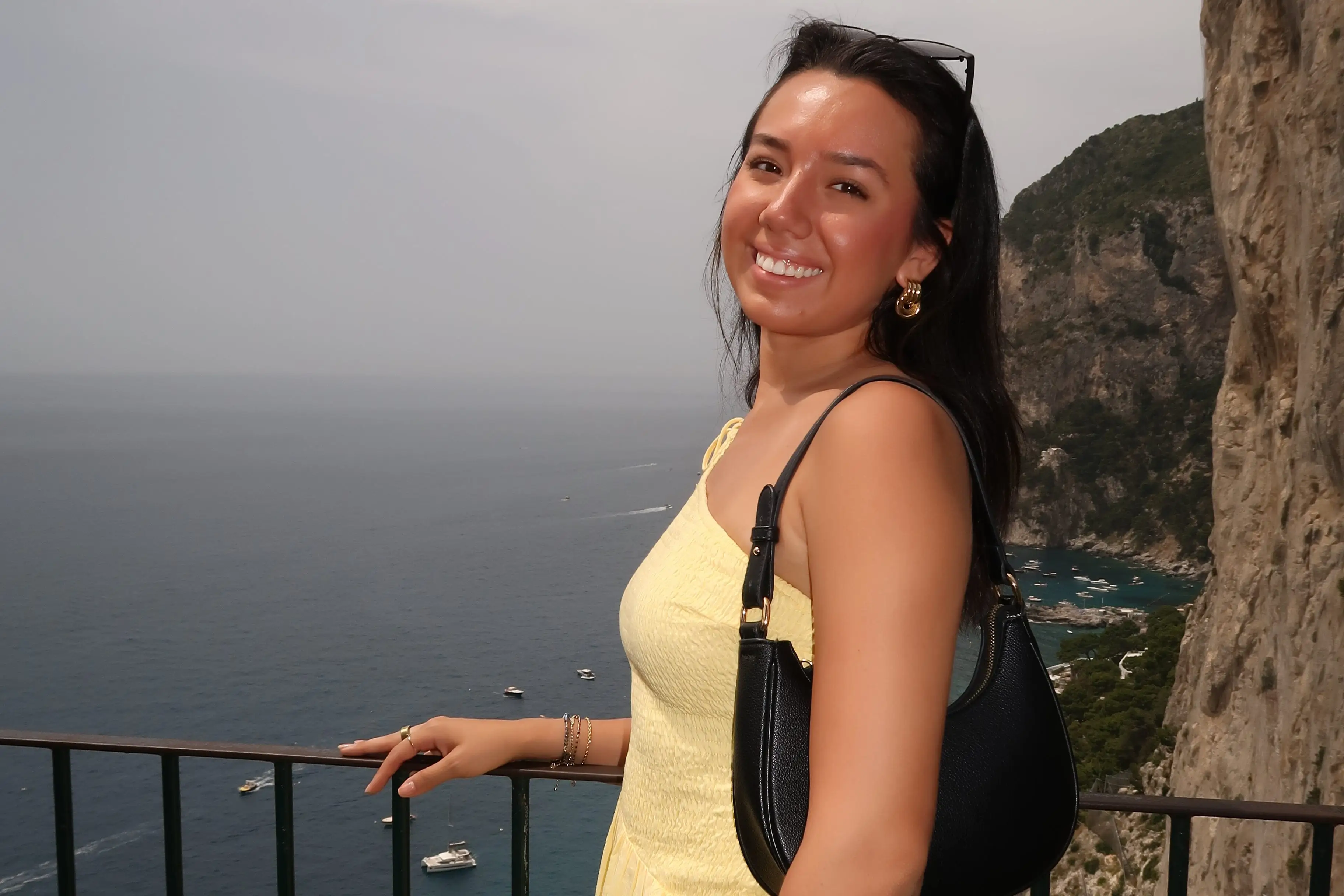 A woman smiling near a rail overlooking a mountain and the sea.