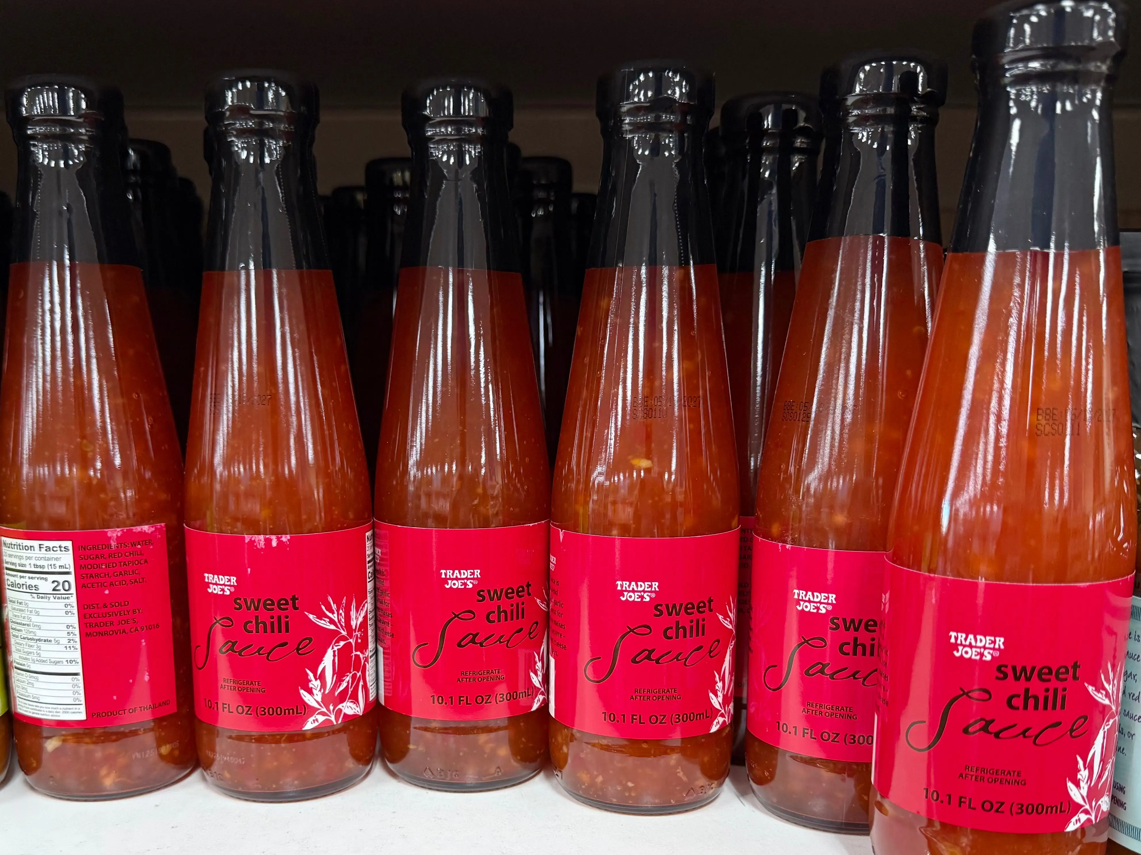 Several bottles of Trader Joe's sweet chili sauce sitting on a shelf.
