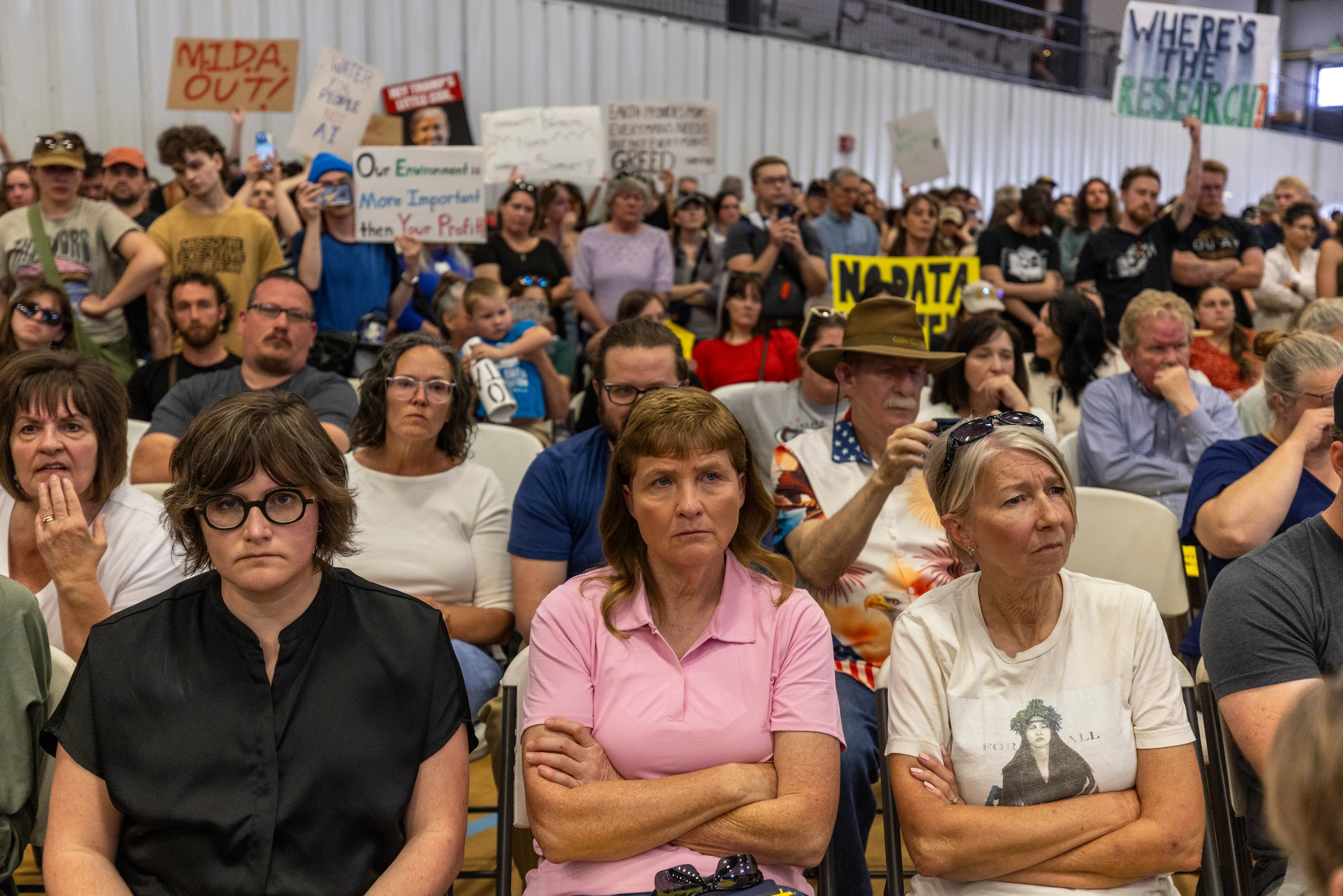 Grim-faced residents seated in front of sign-holding protesters.