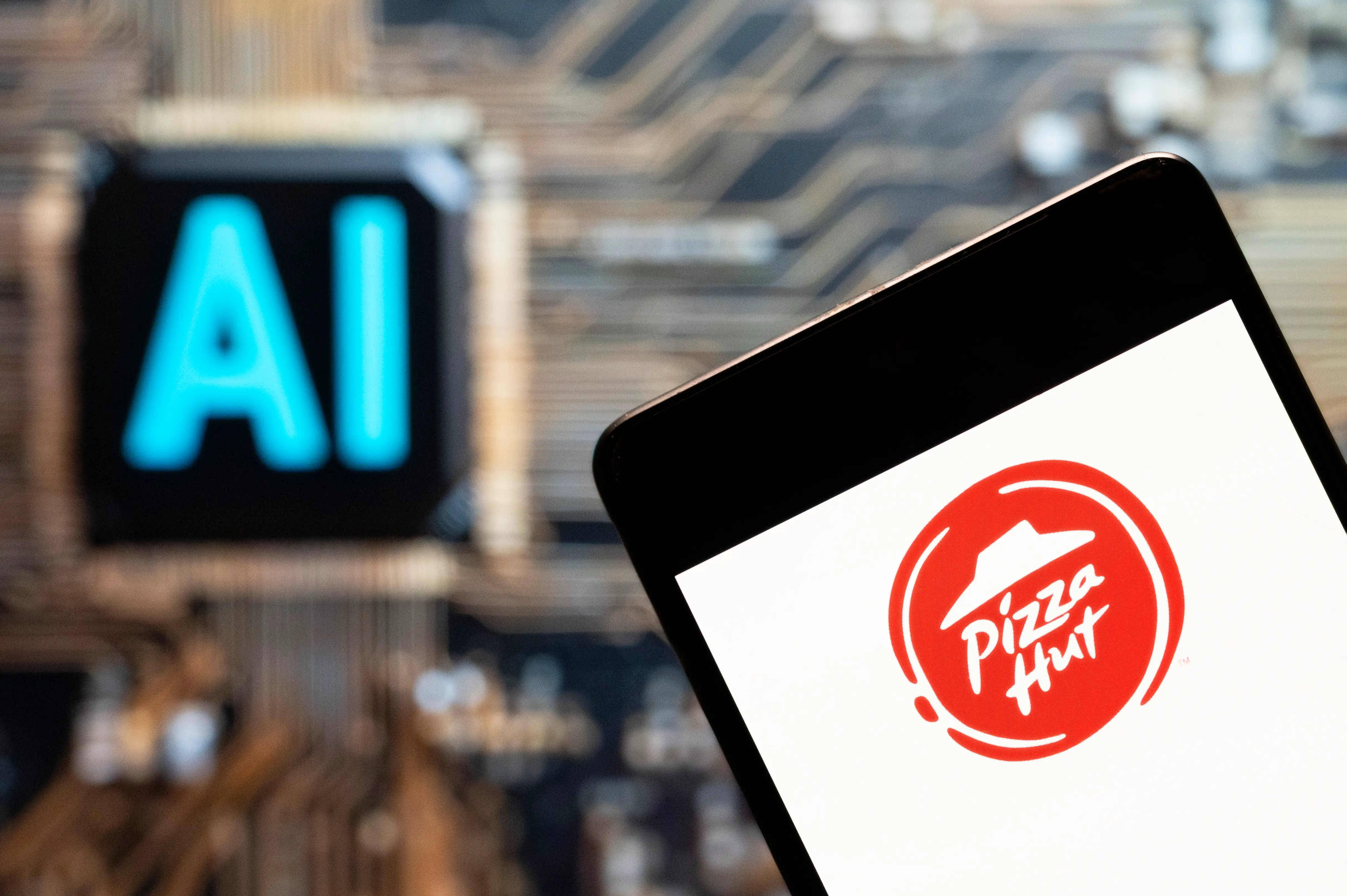 A Pizza Hut logo appears on a smartphone in front of an illuminated AI chip.