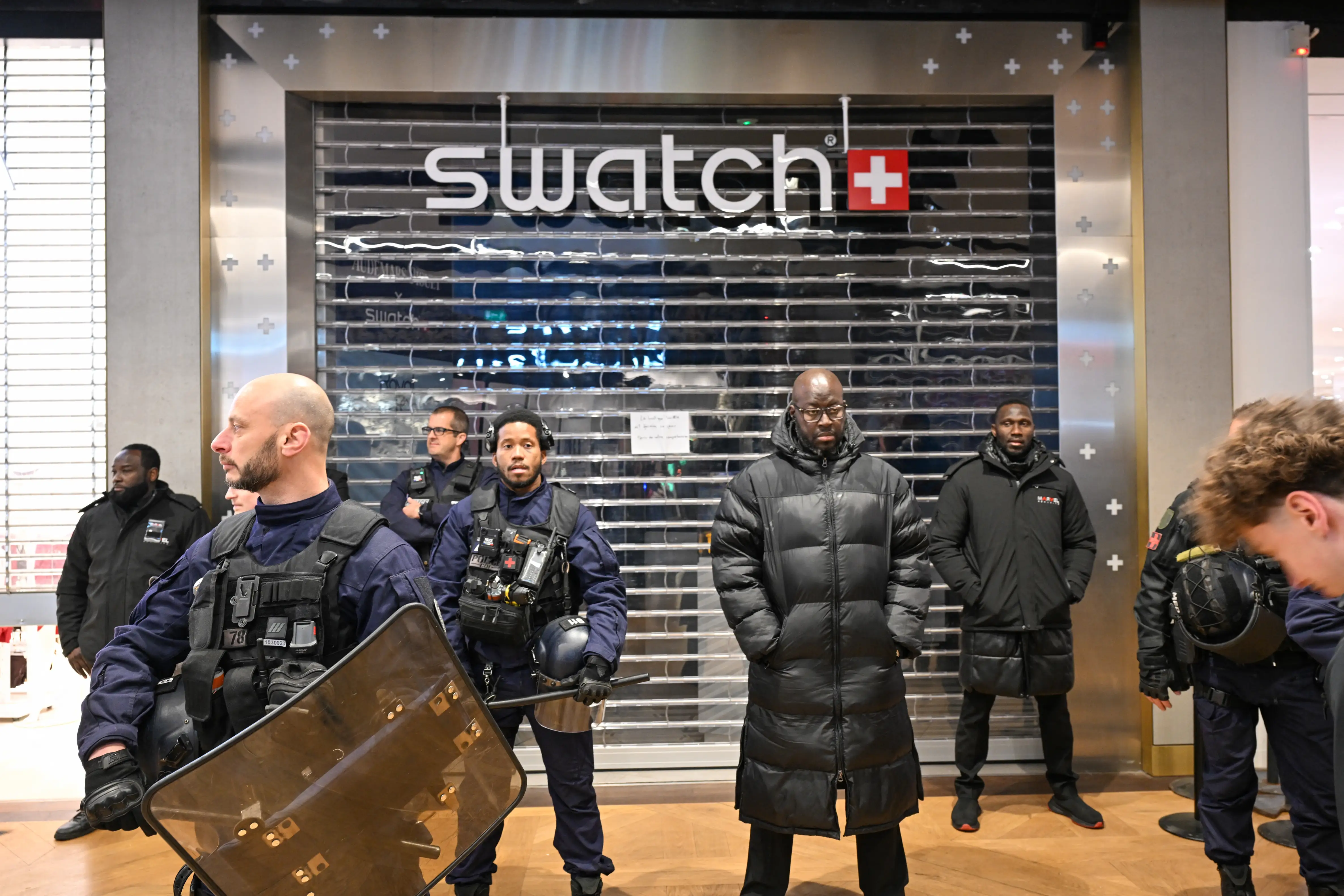 Riot police stand in front of a Swatch store