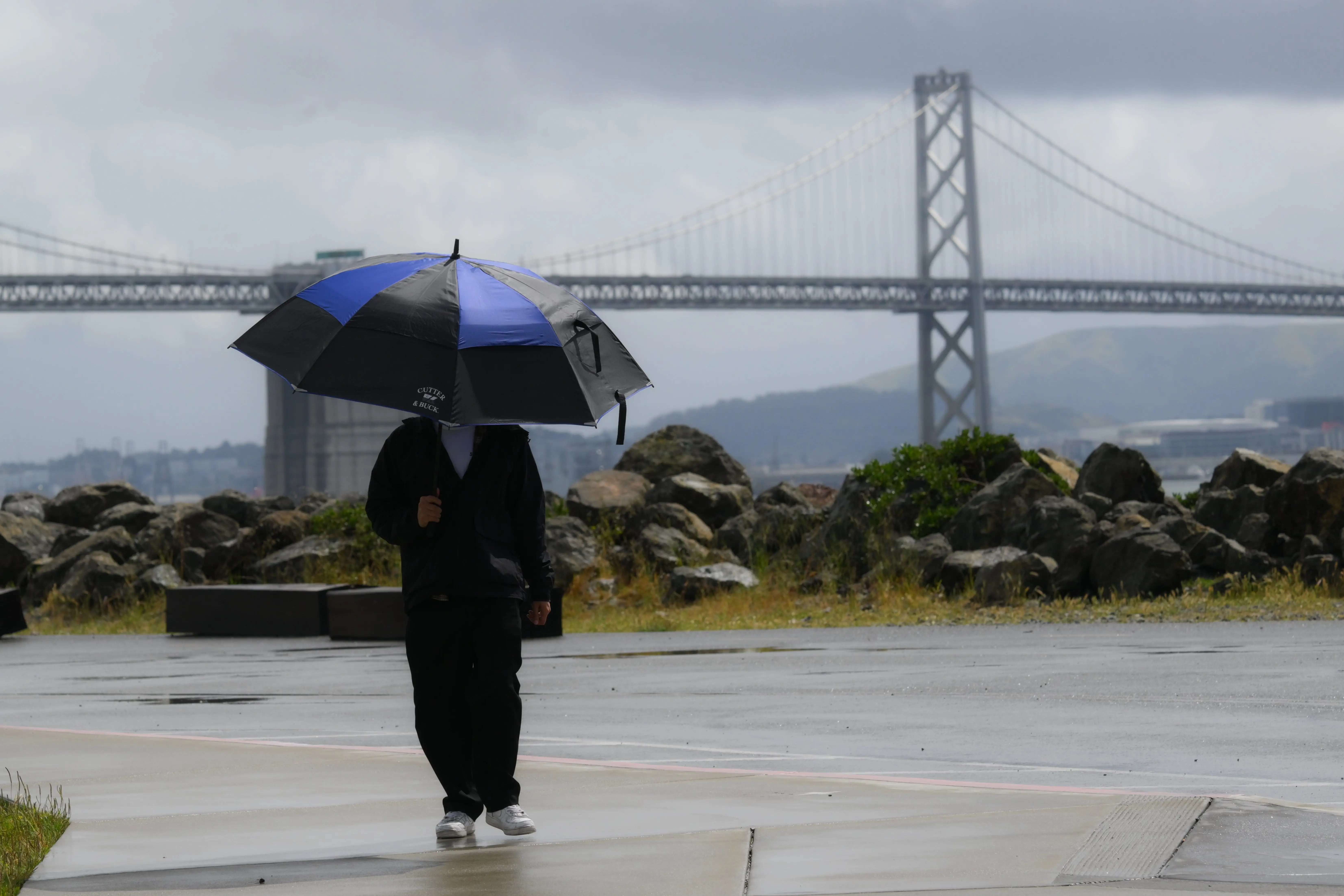 A man with an umbrella walks in front of the Golden Gate Bridge