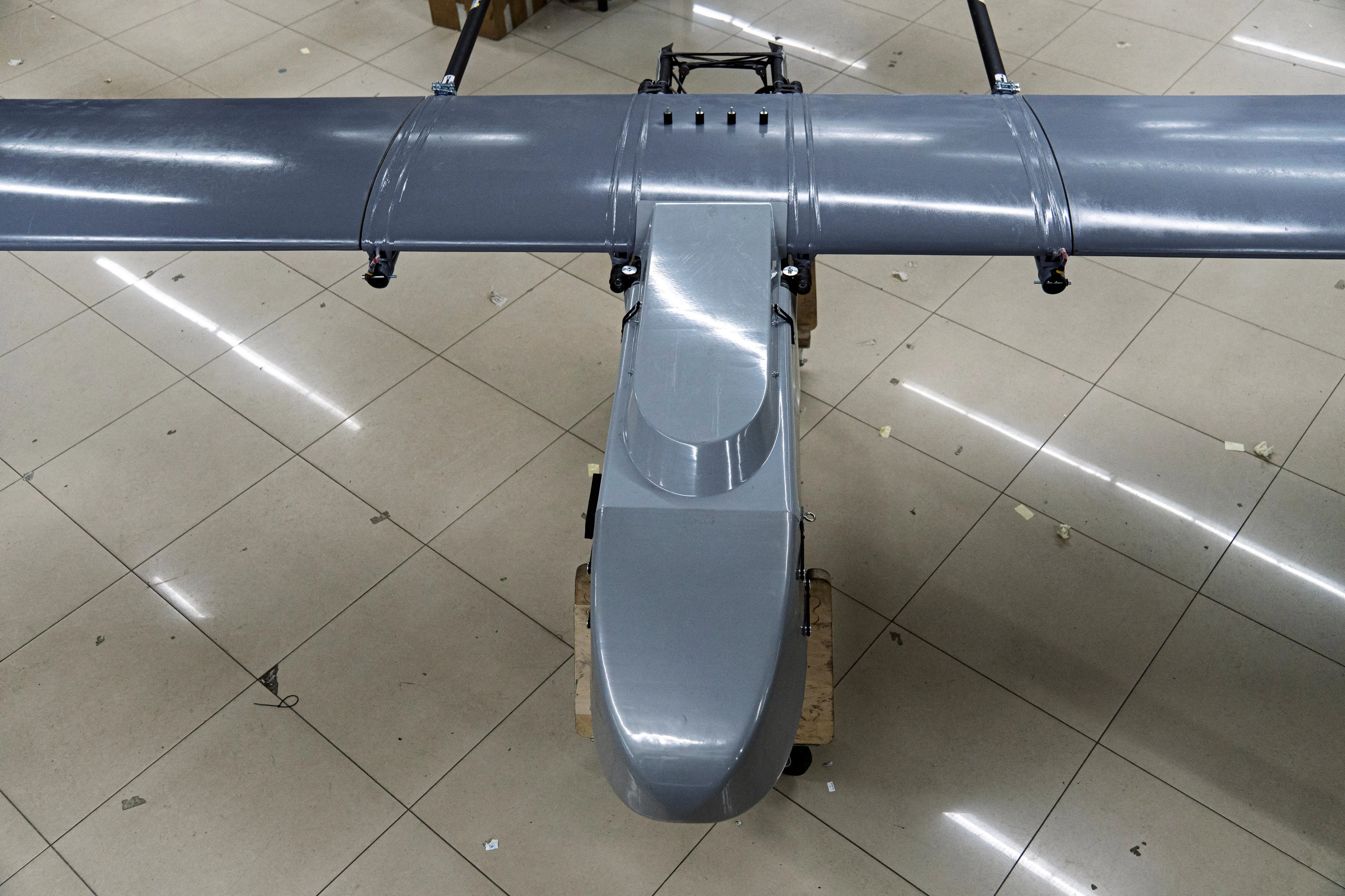 A long-range fixed wing drone sits on a factory production floor.