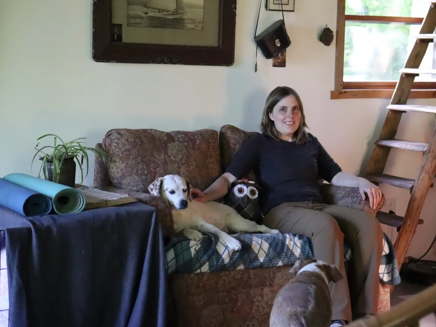 The writer sitting on a small couch next to a dog in her cabin.