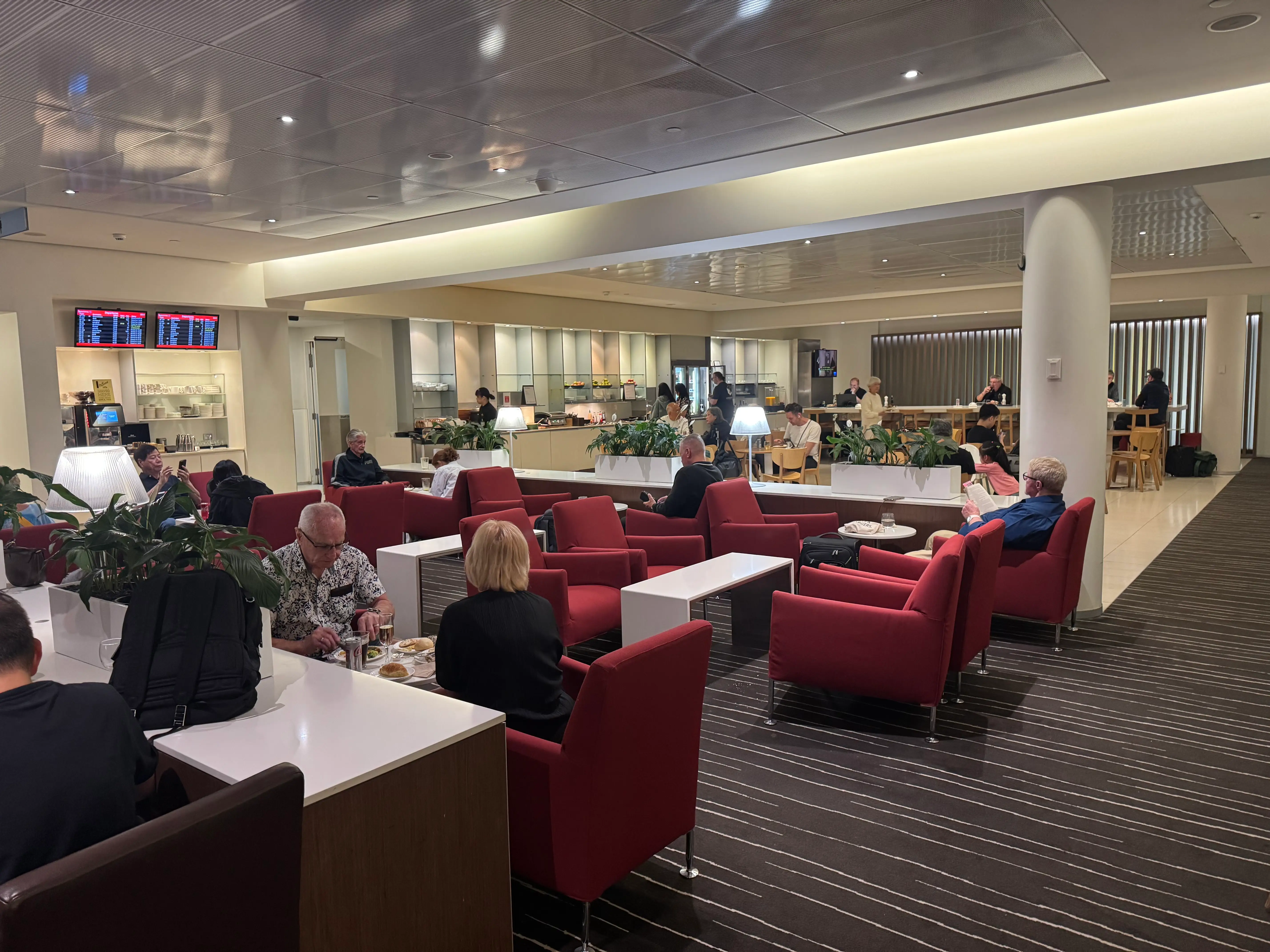 People in business class lounge with red chairs, eating area