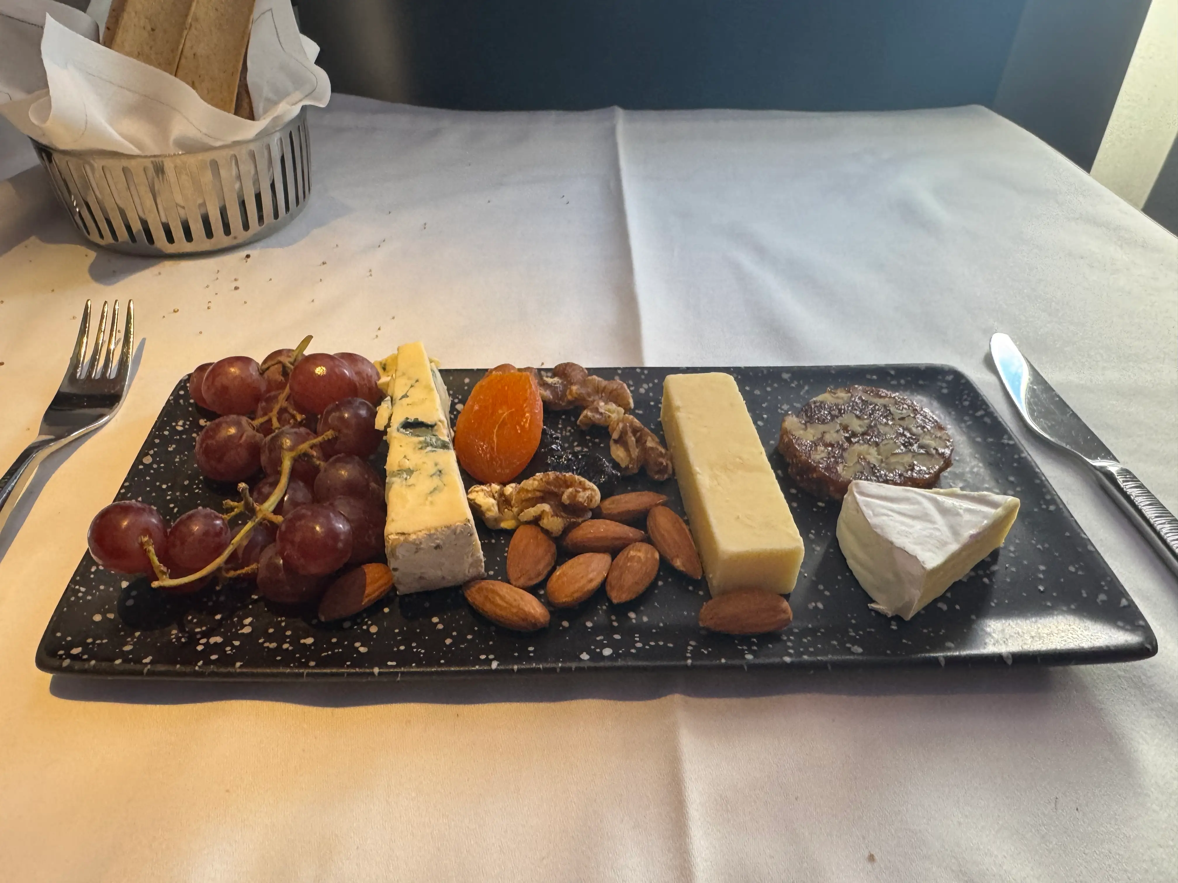 cheeseboard on white tablecloth-covered tray table in Q Suite in flight