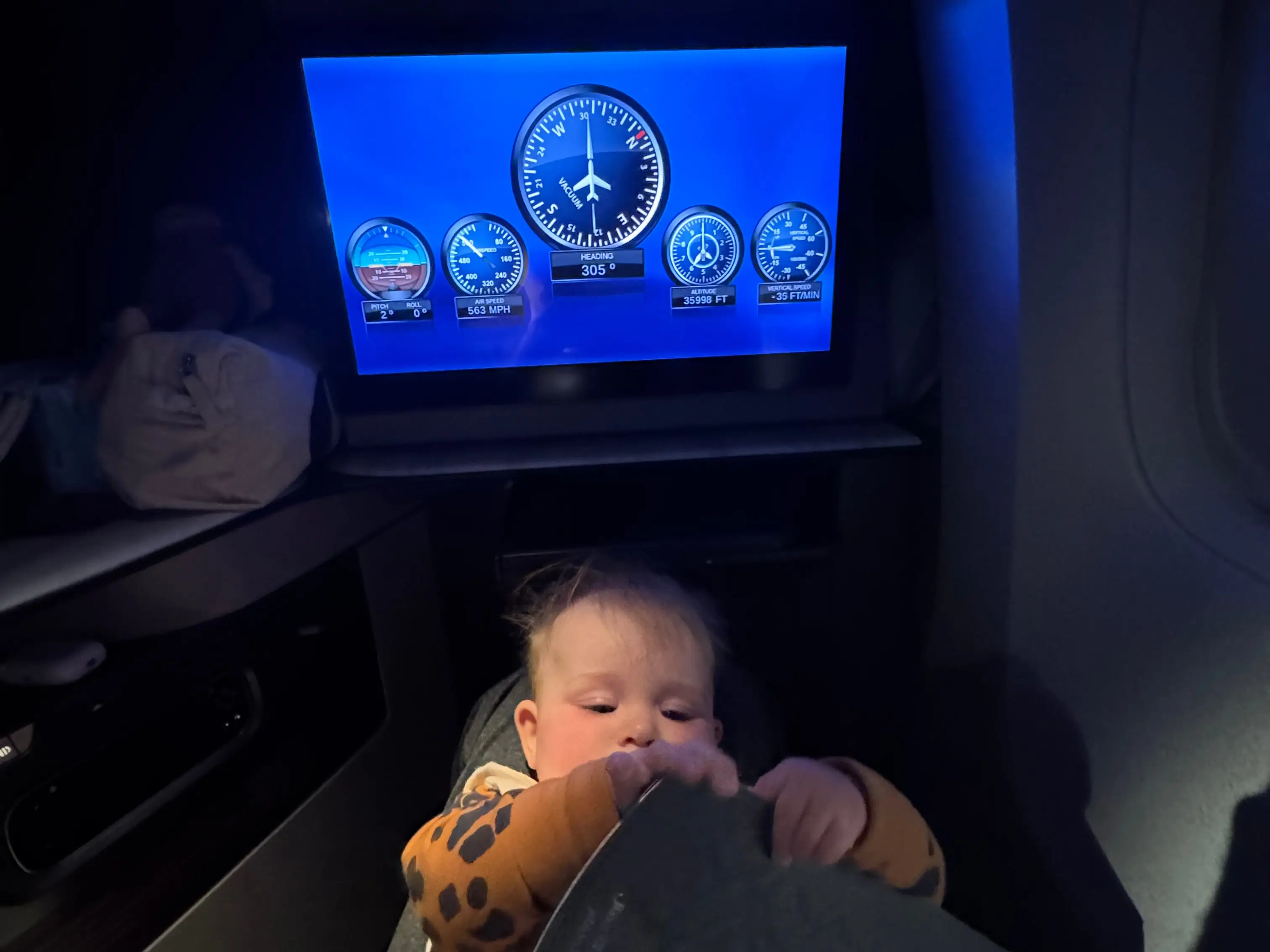 seatback screen on flight above baby lying on person's lap
