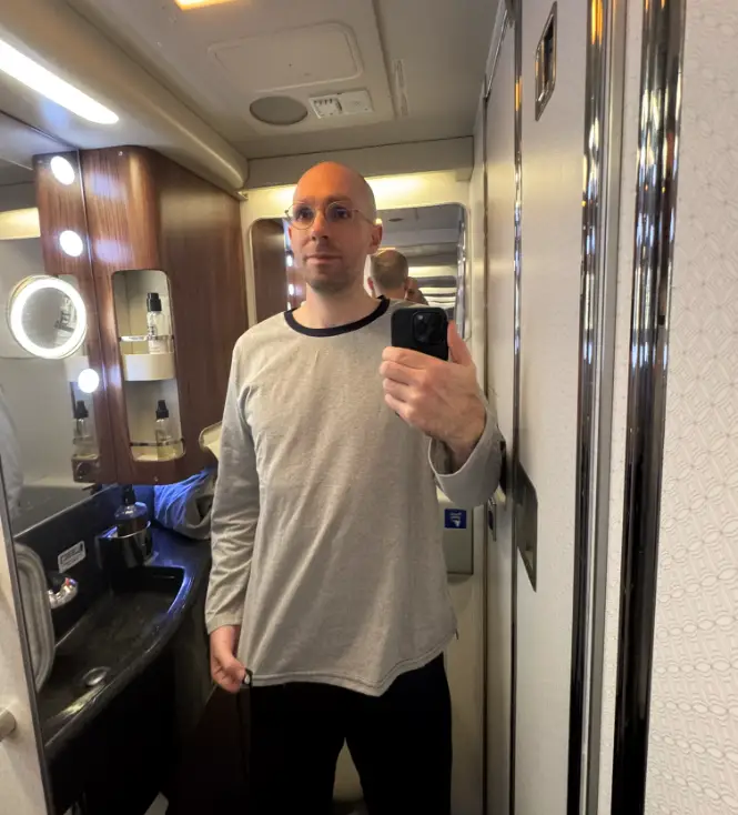 Man taking selfie in plain bathroom in Qatar Airways pajamas
