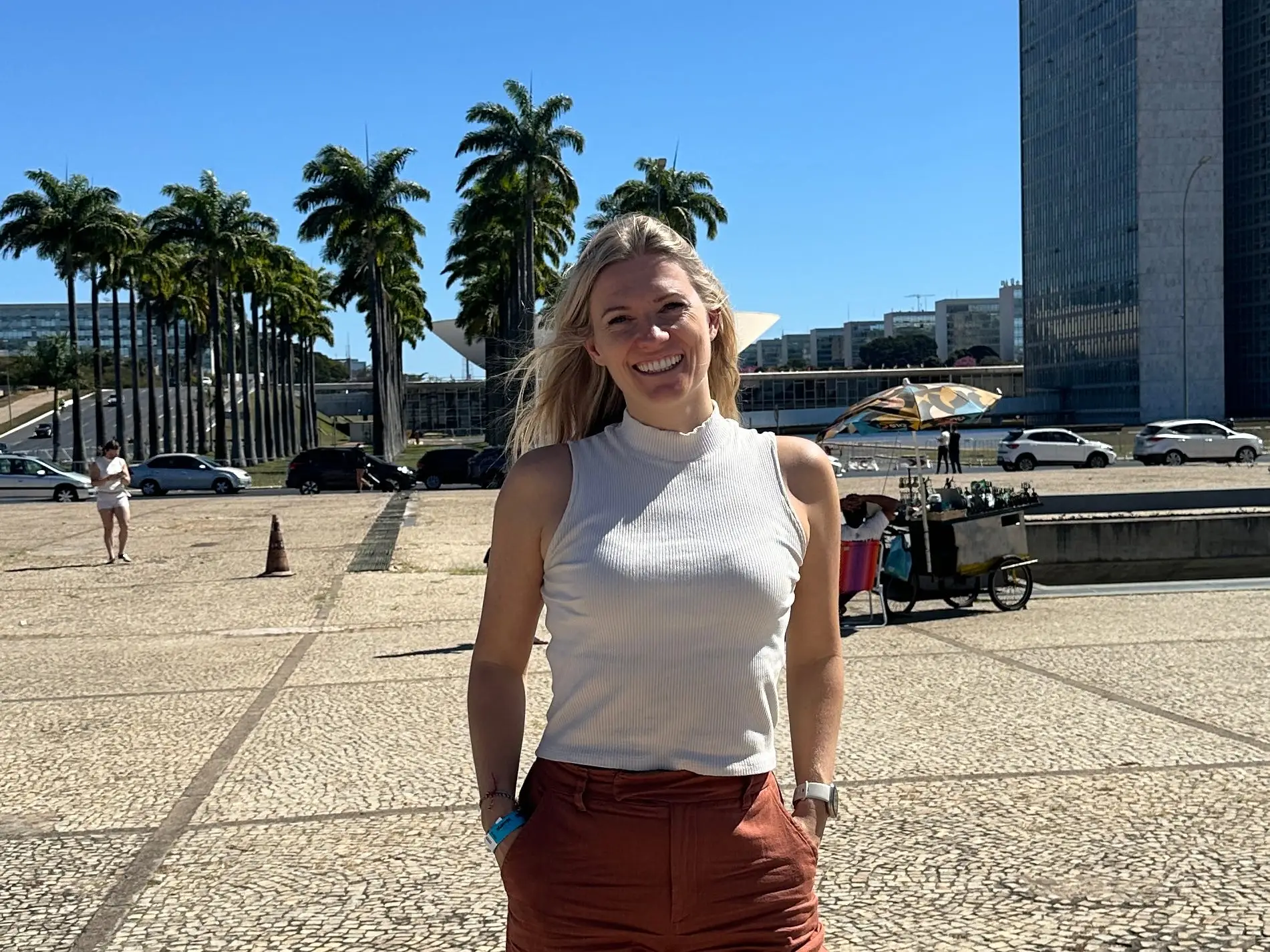 A woman posing with the National Congress building in Brasilia, Brazil, in the background.