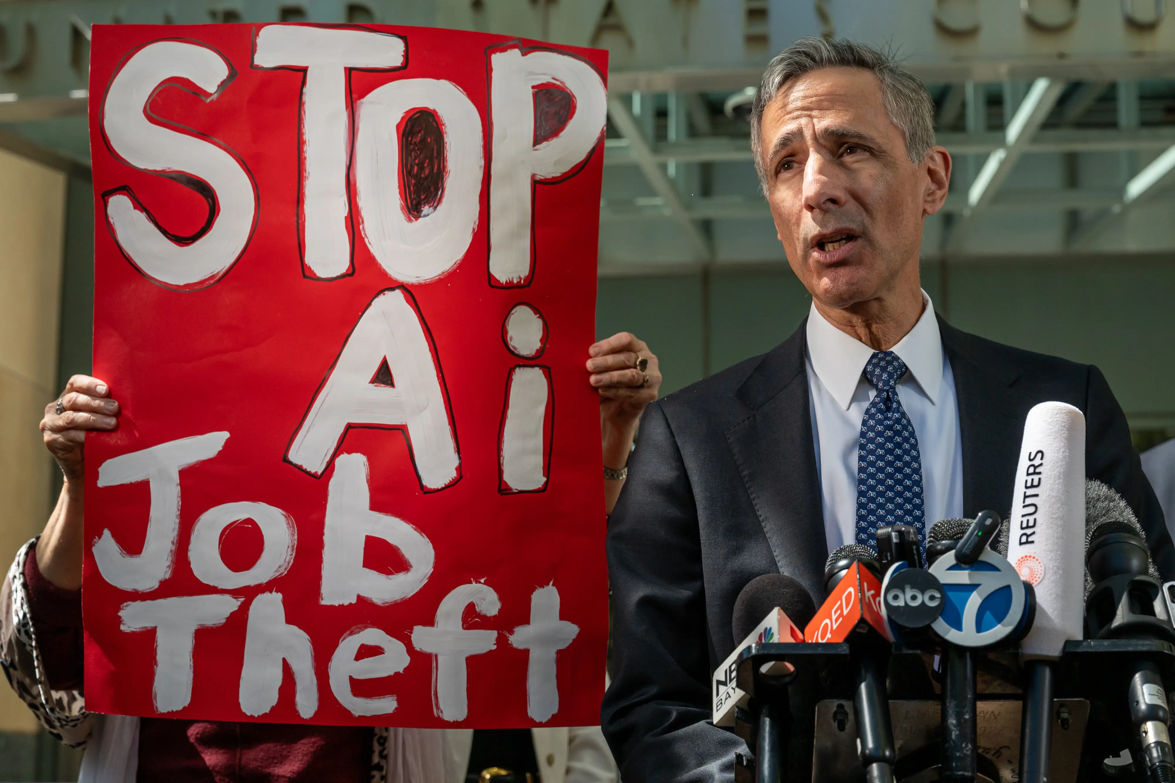 Attorney William Savitt, representing OpenAI, speaks during a news conference outside federal court in Oakland, California, with a sign reading 
