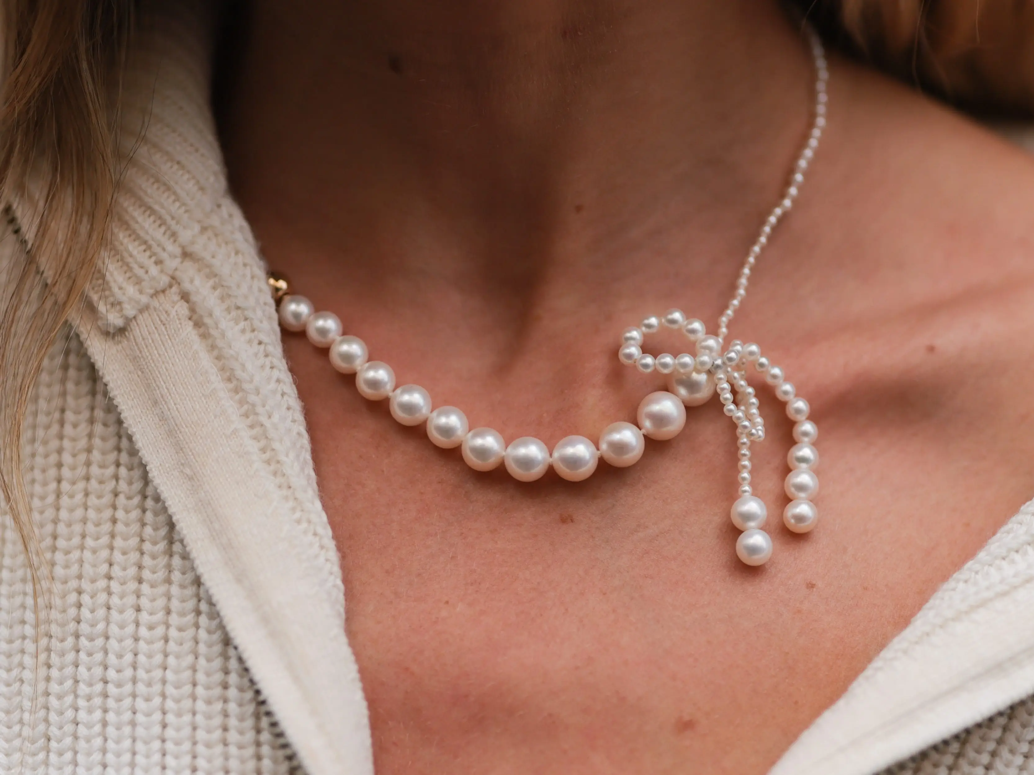 A woman wearing a pearl necklace shaped like a bow.