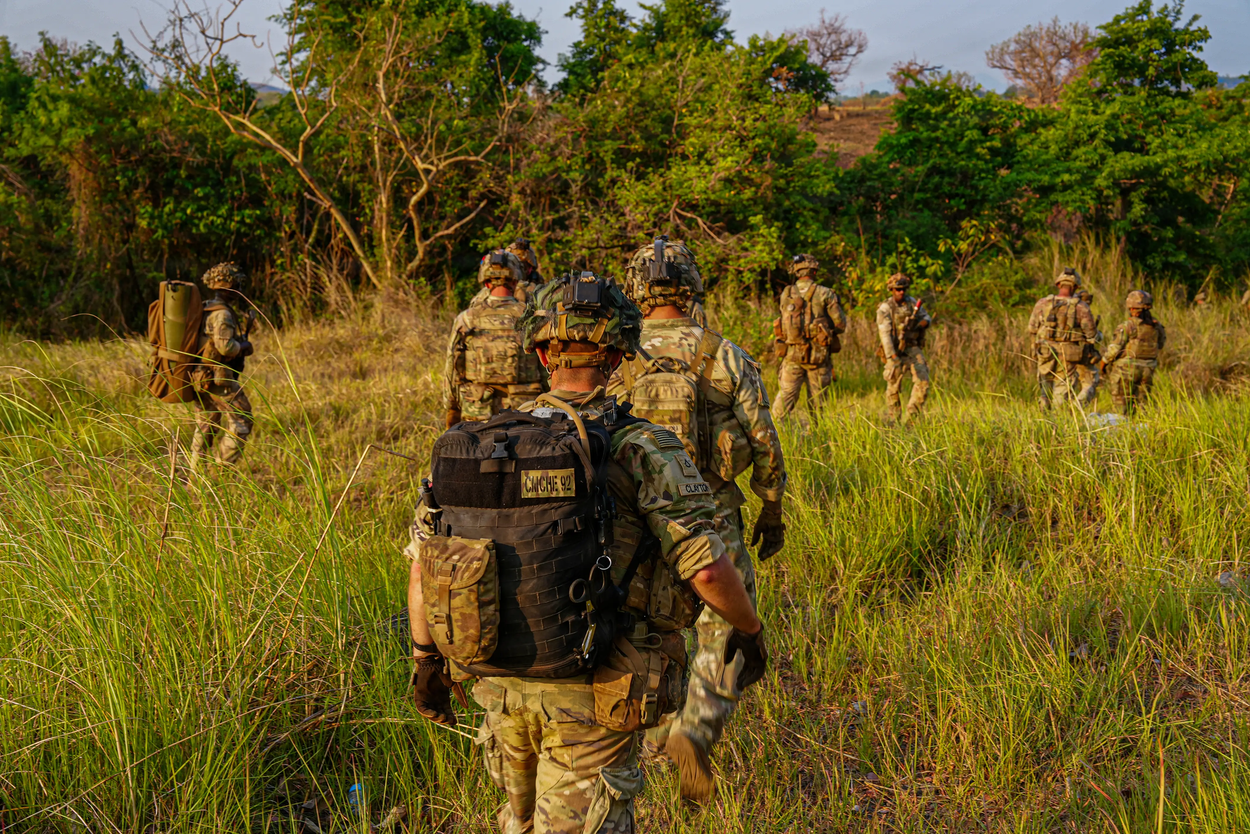 Soldiers wearing camouflage walk in tall green grass in the jungle.