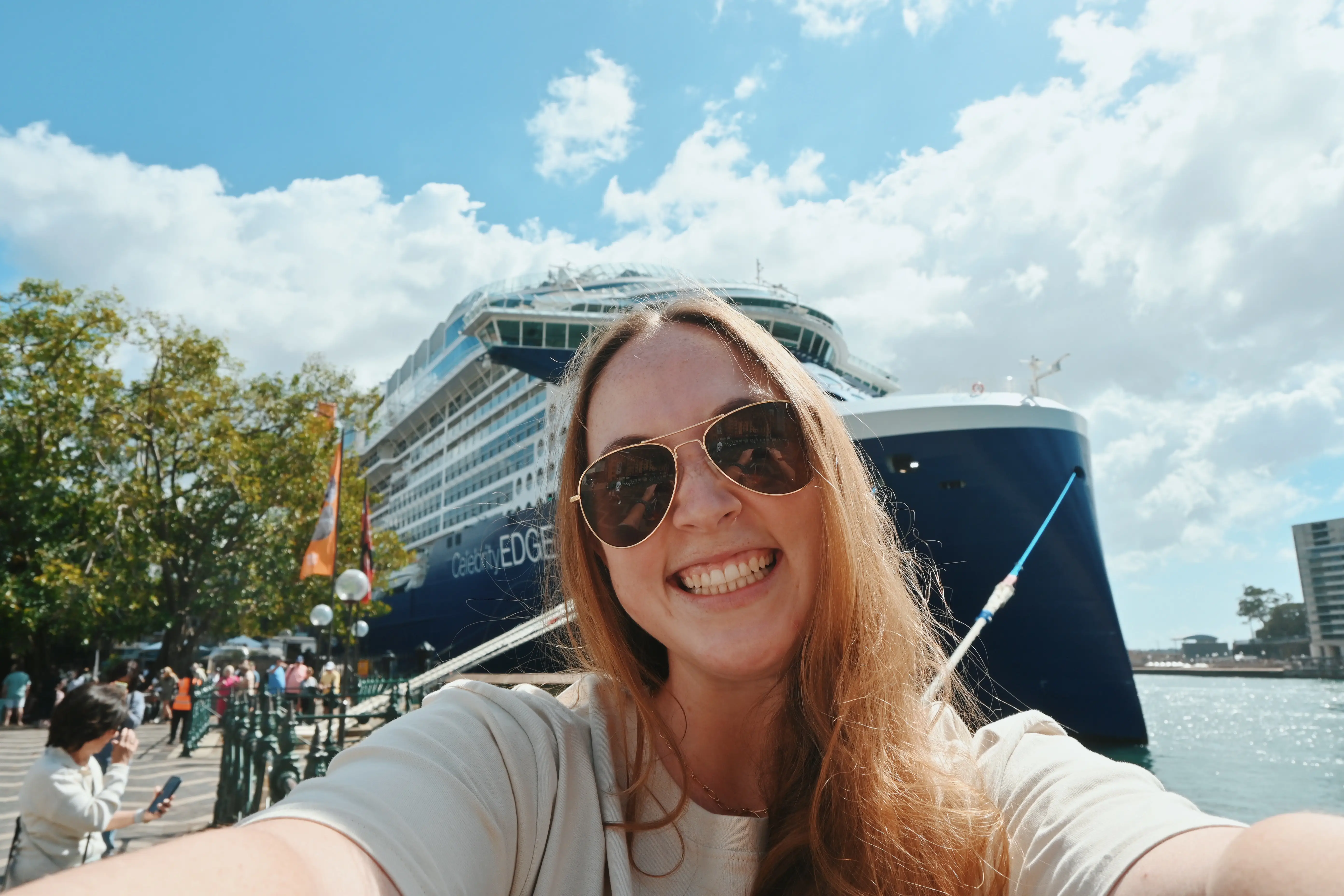 Author Allie Hubers smiling in front of Celebrity Edge cruise ship, taking selfie