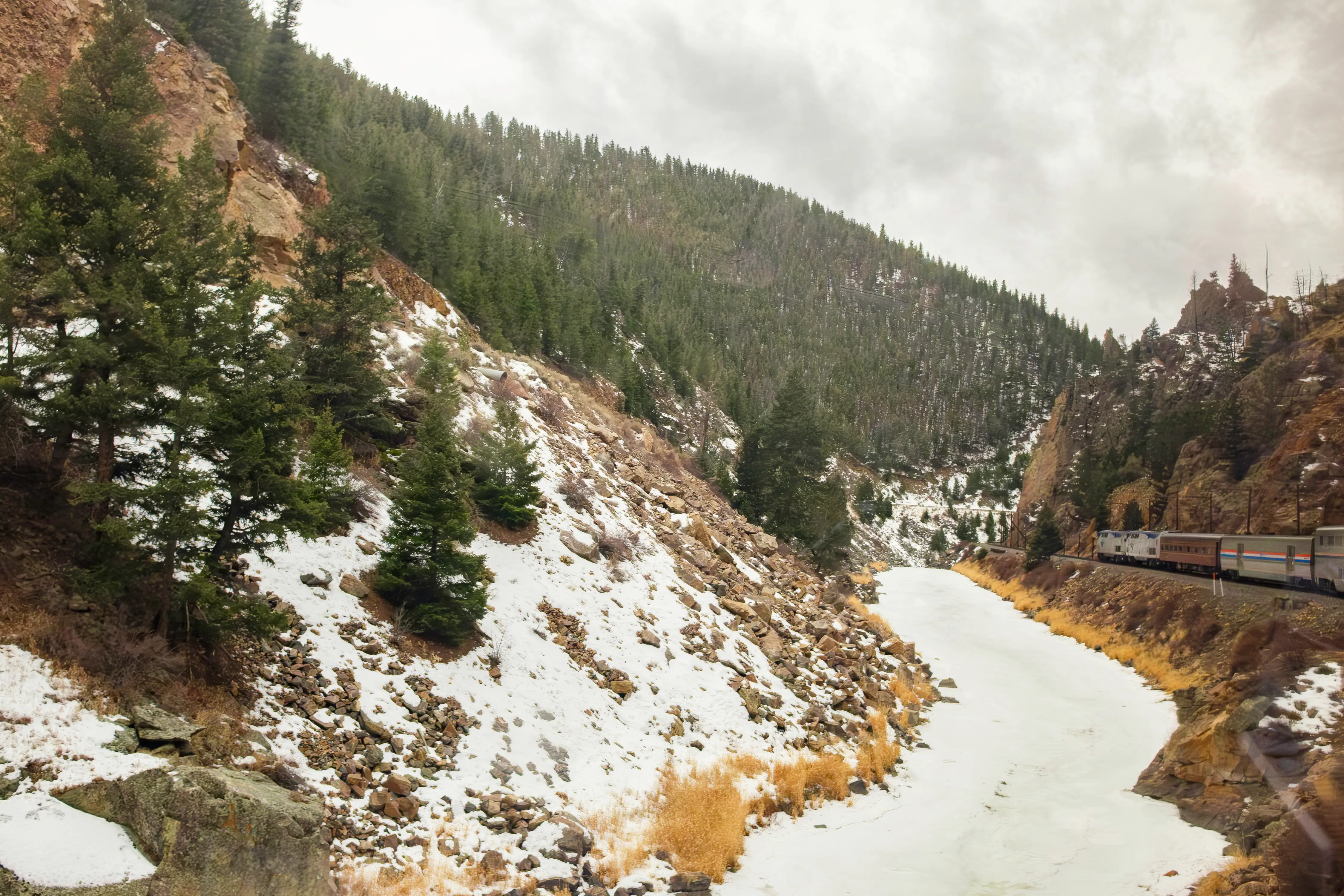 A train on the right side of a snowy mountain scene