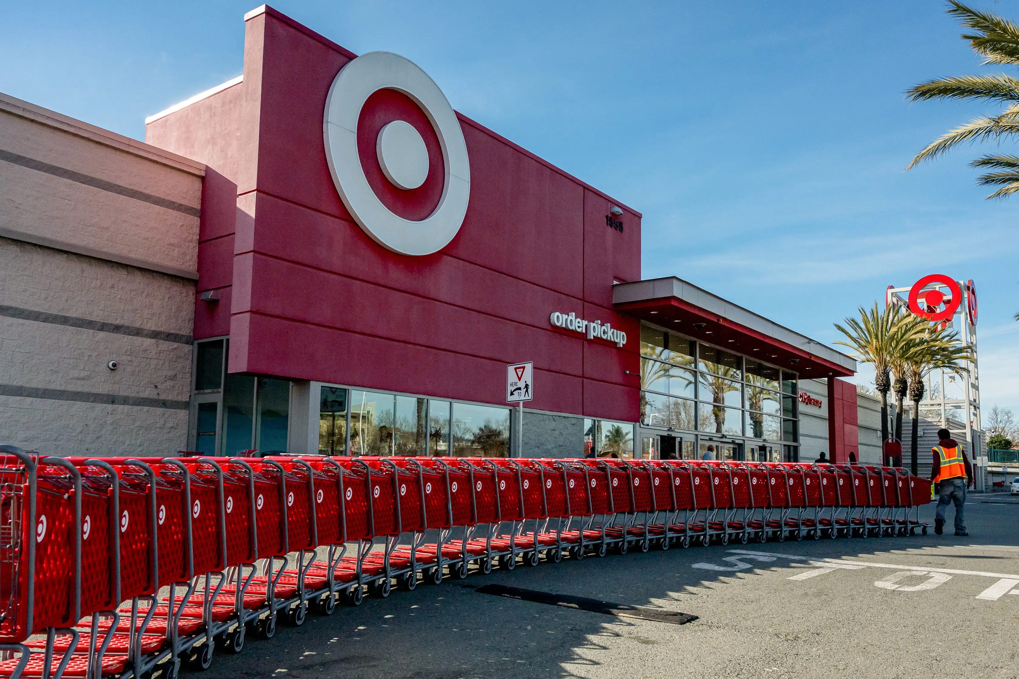 A cart attendant pulls a line of red carts toward the front doors of a Target store.