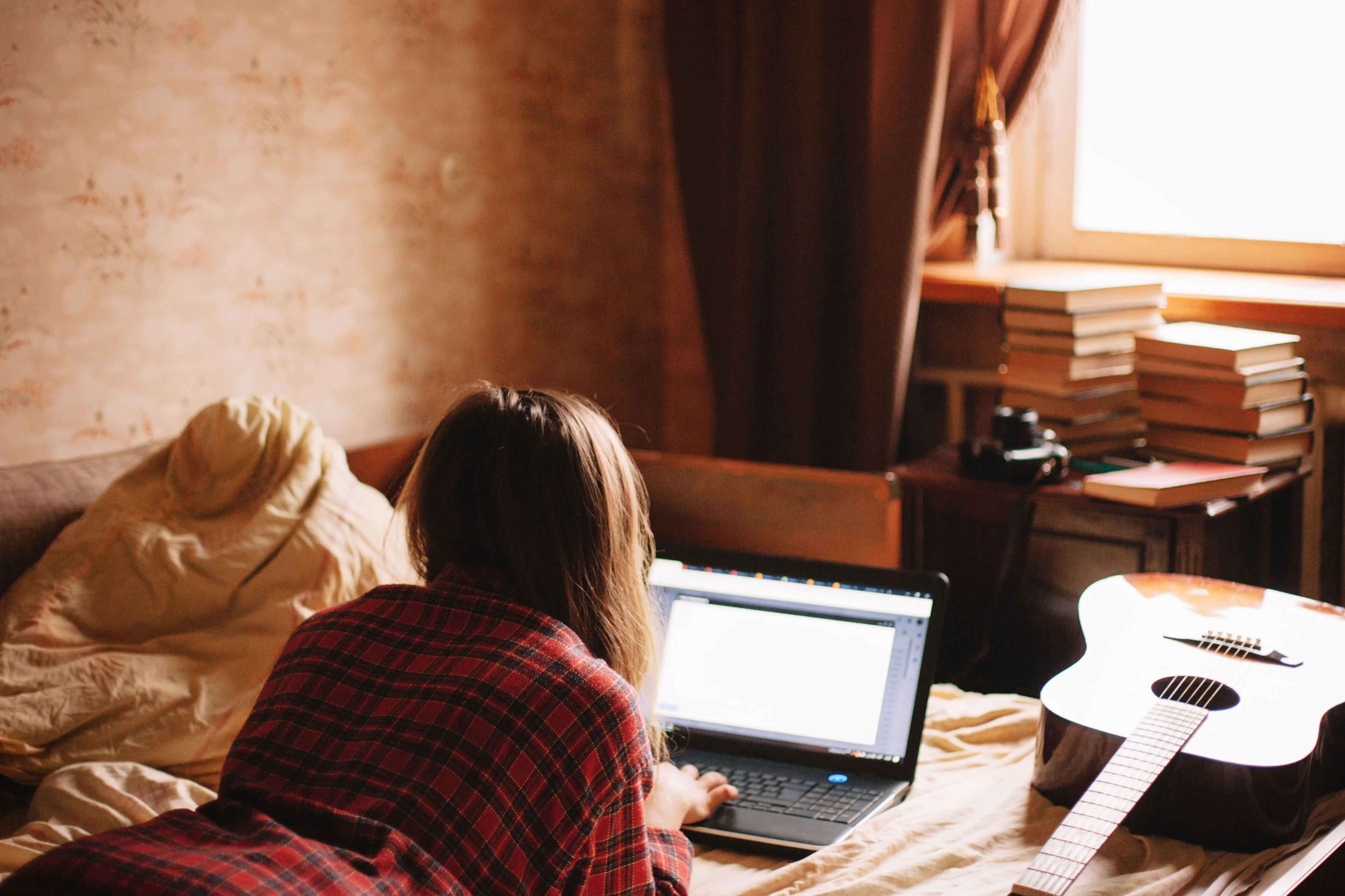 Young woman using laptop while lying on bed at home - stock photo