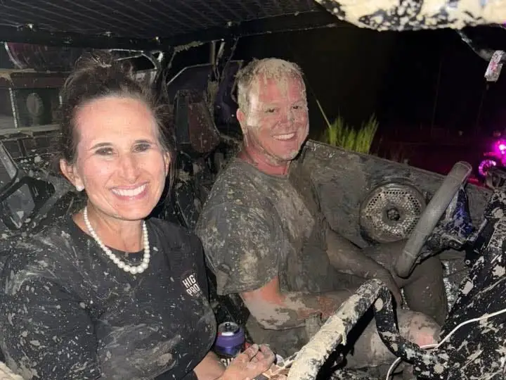 A couple going off-roading on side-by-sides through the mud.