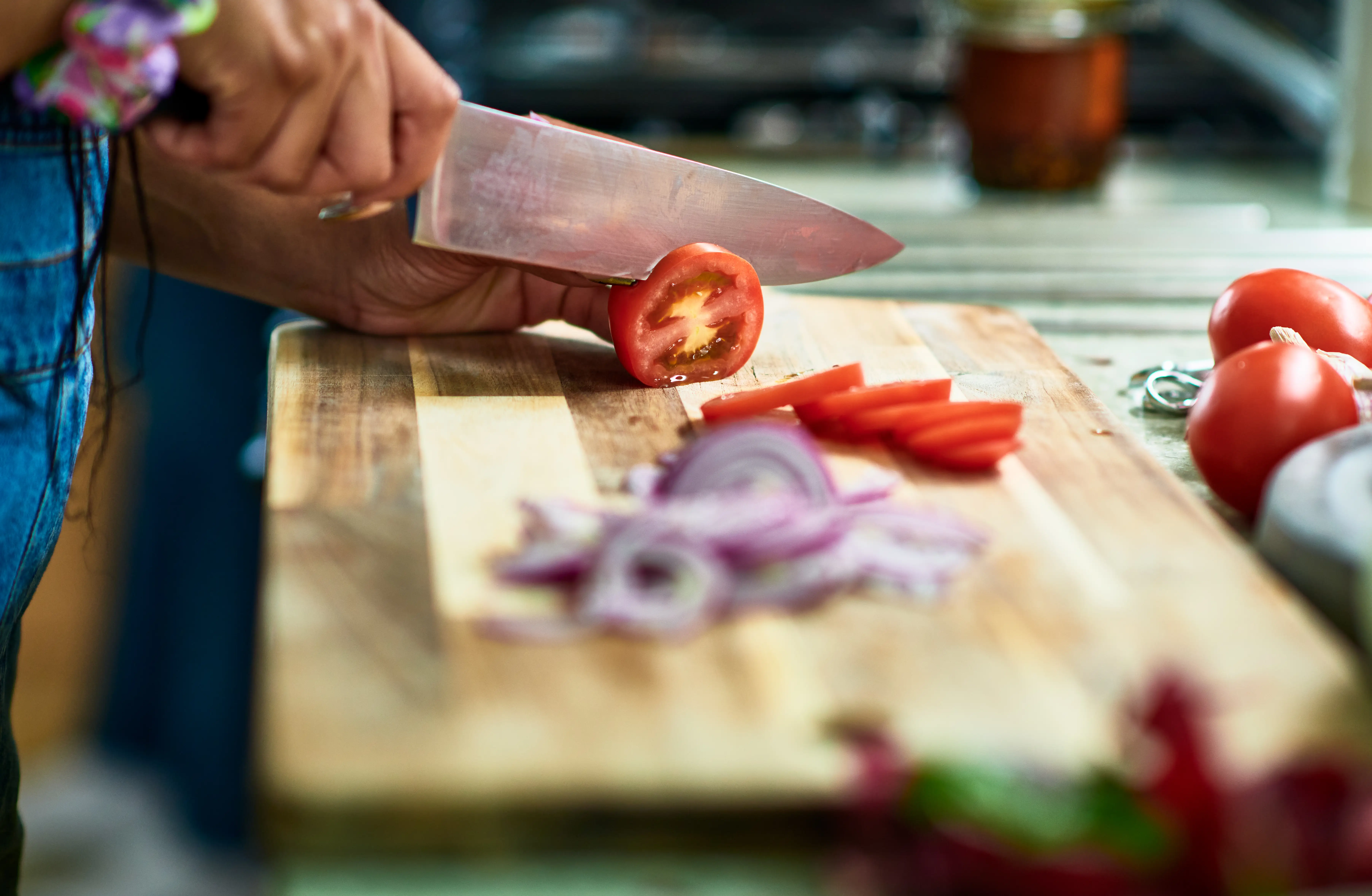 Photo of hand slicing a tomato on a wooden cutting board