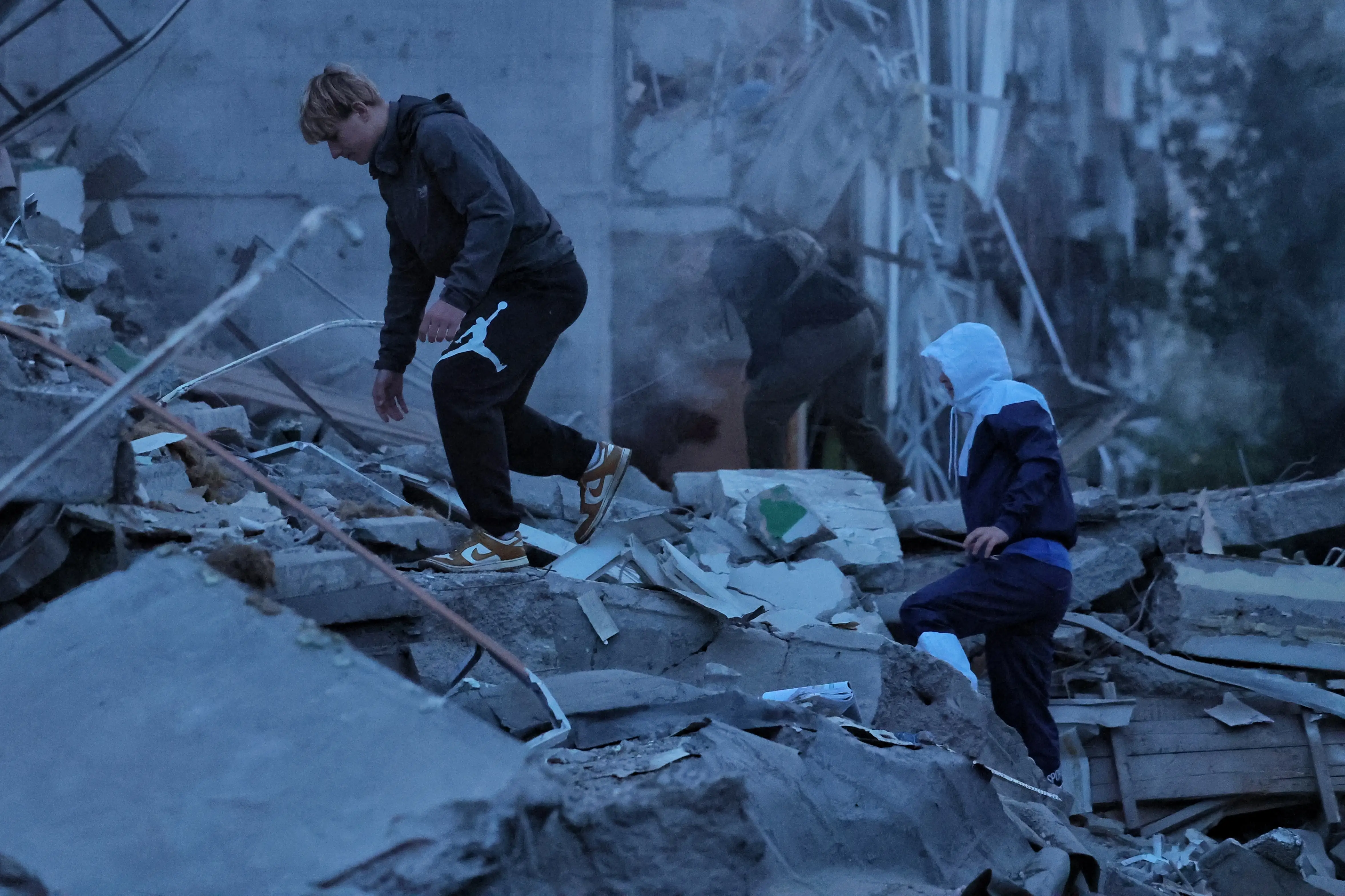Two men in dark tracksuits walk over large pieces of rubble