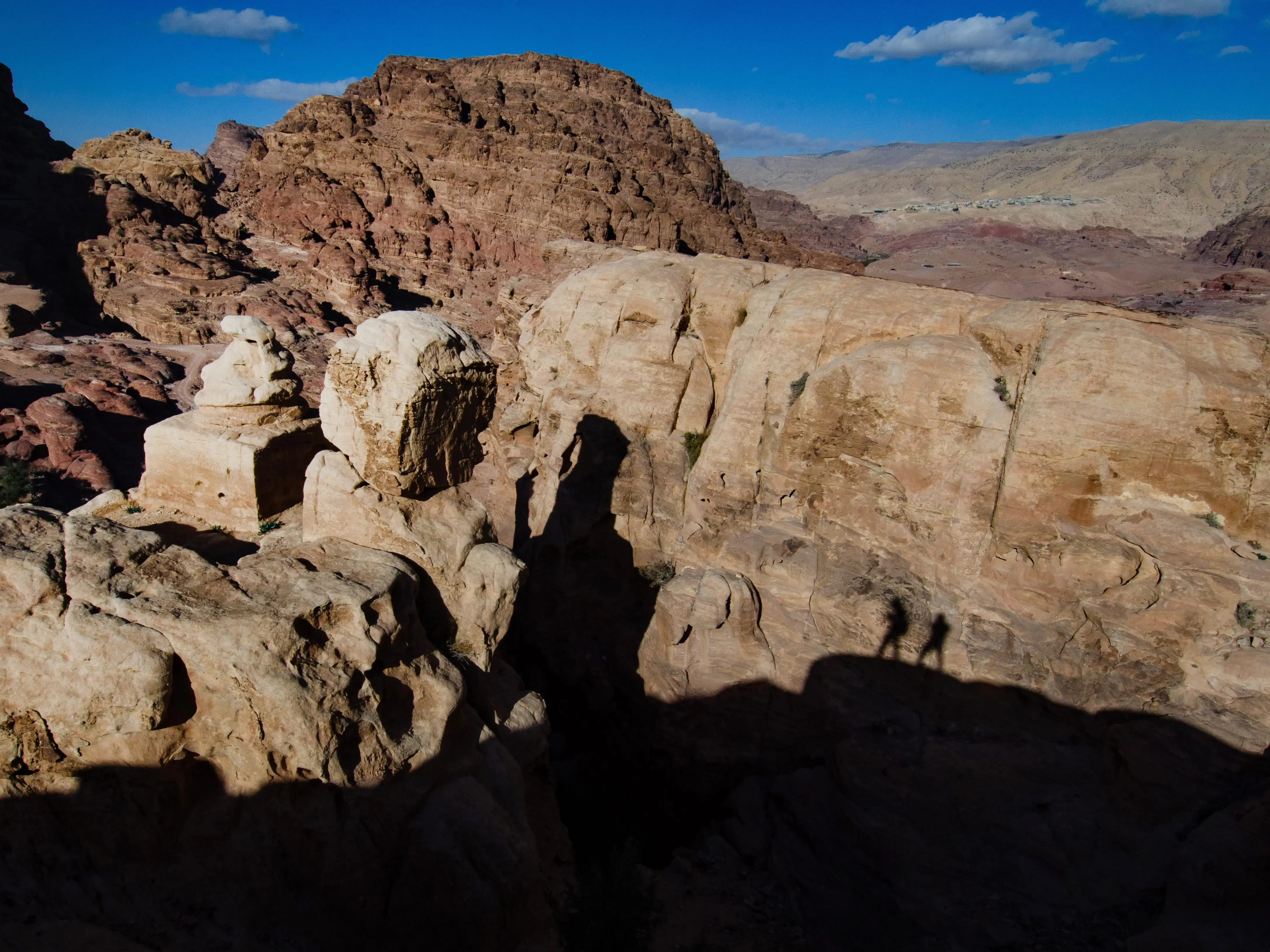 Shadows of several people hiking along the rocky terrain of Petra, Jordan.