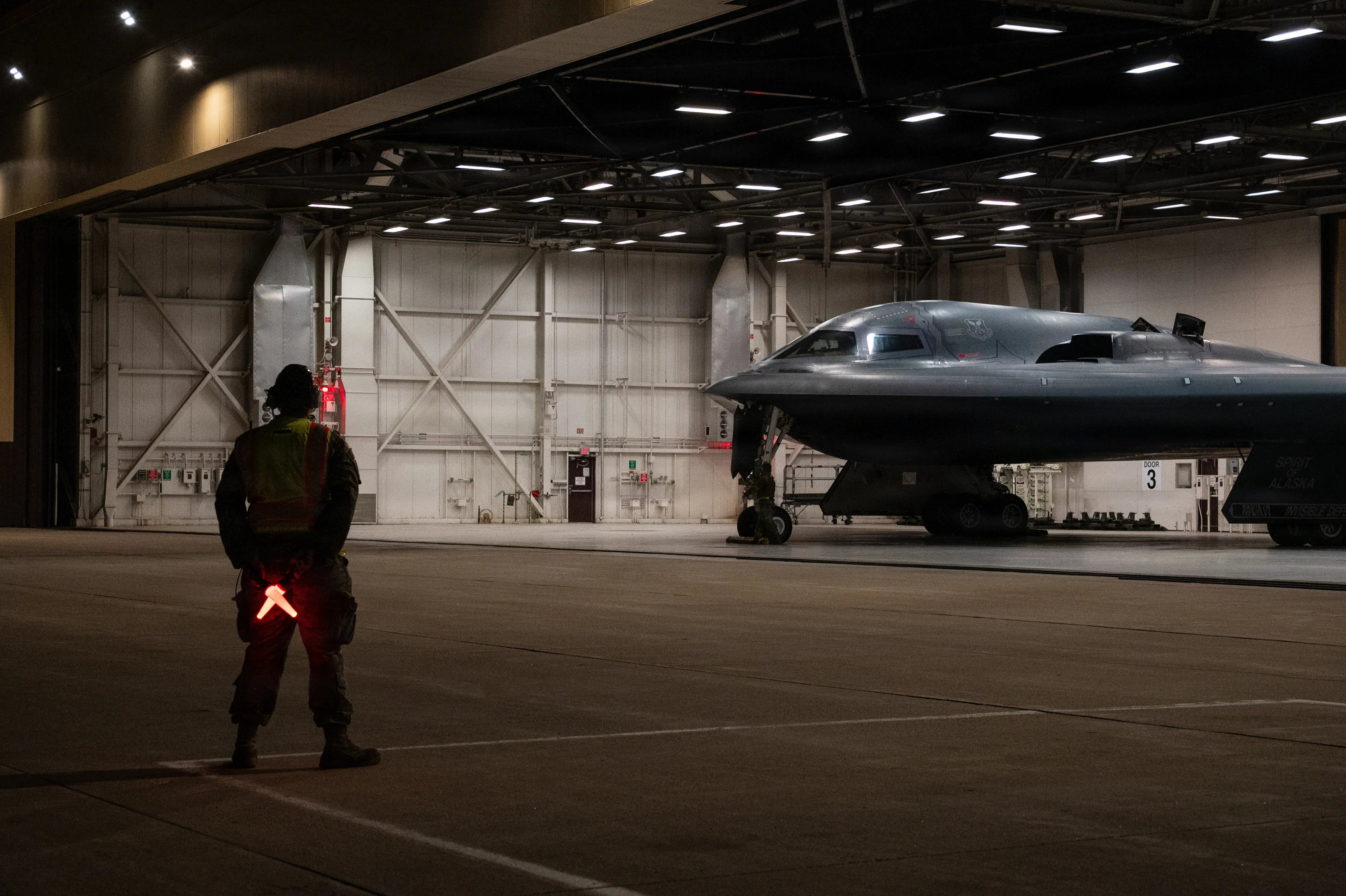 A US Air Force B-2 Spirit bomber sits in a garage. A man stands in front of it.