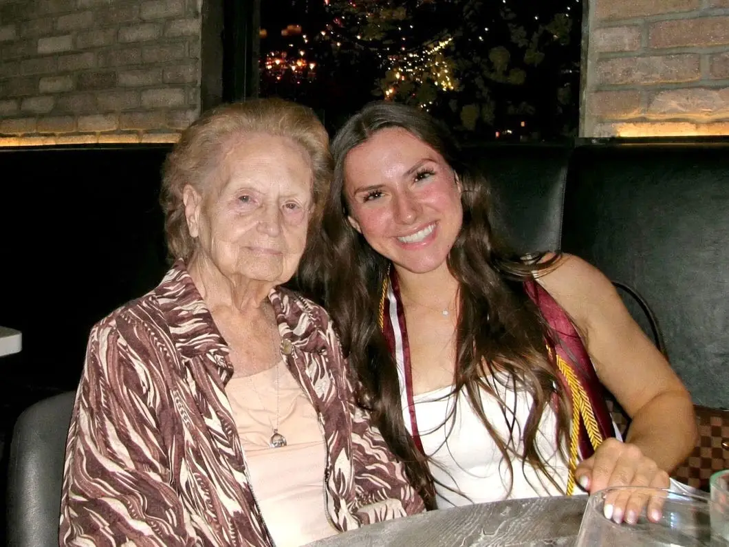 Amanda and her grandma sit at a table and smile for a photo.