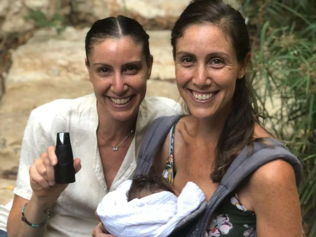 Twin sisters outdoors, one holding a baby and another holding health tech device Lumen