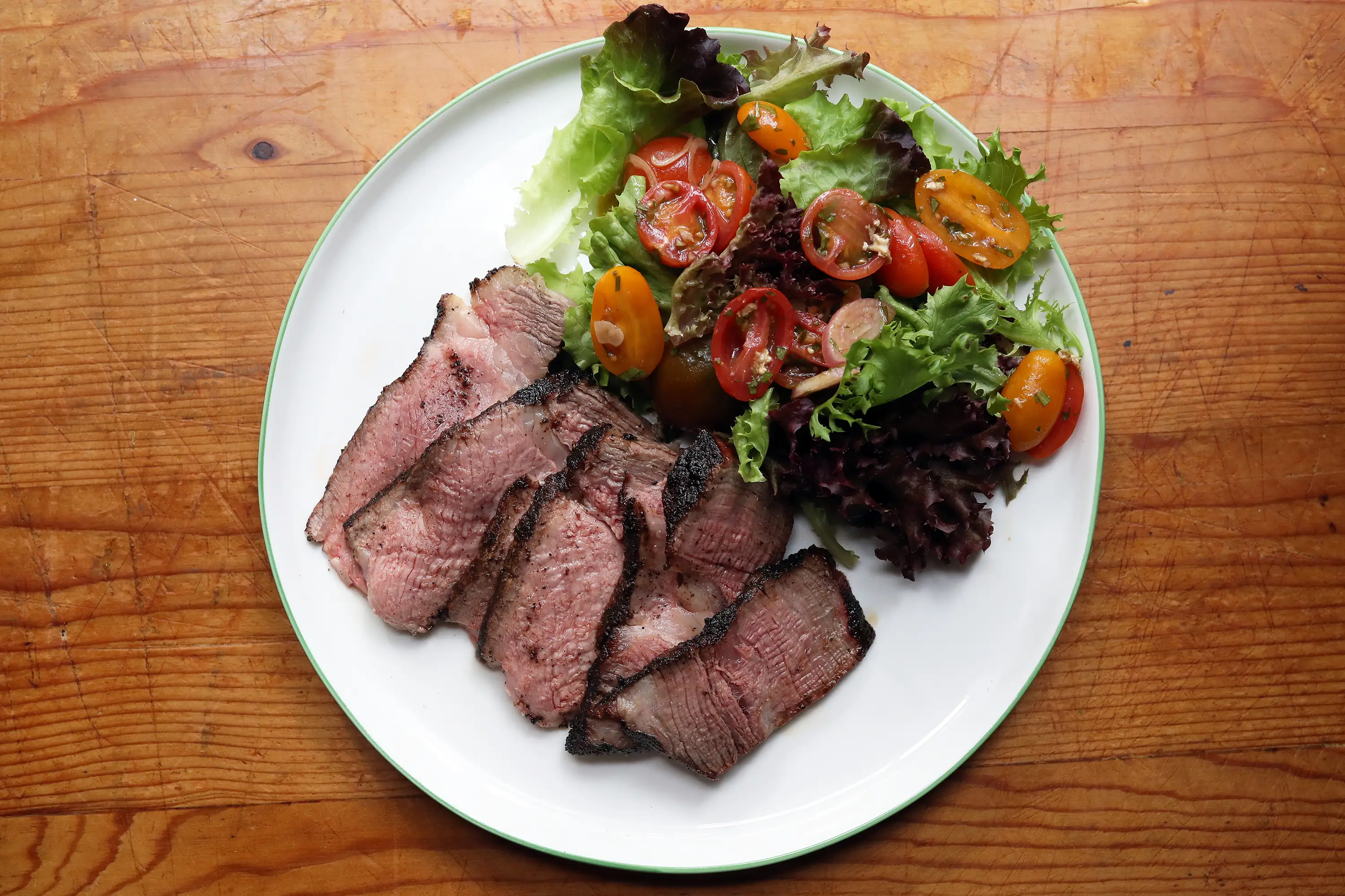 sliced steak on plate next to salad with tomato slices