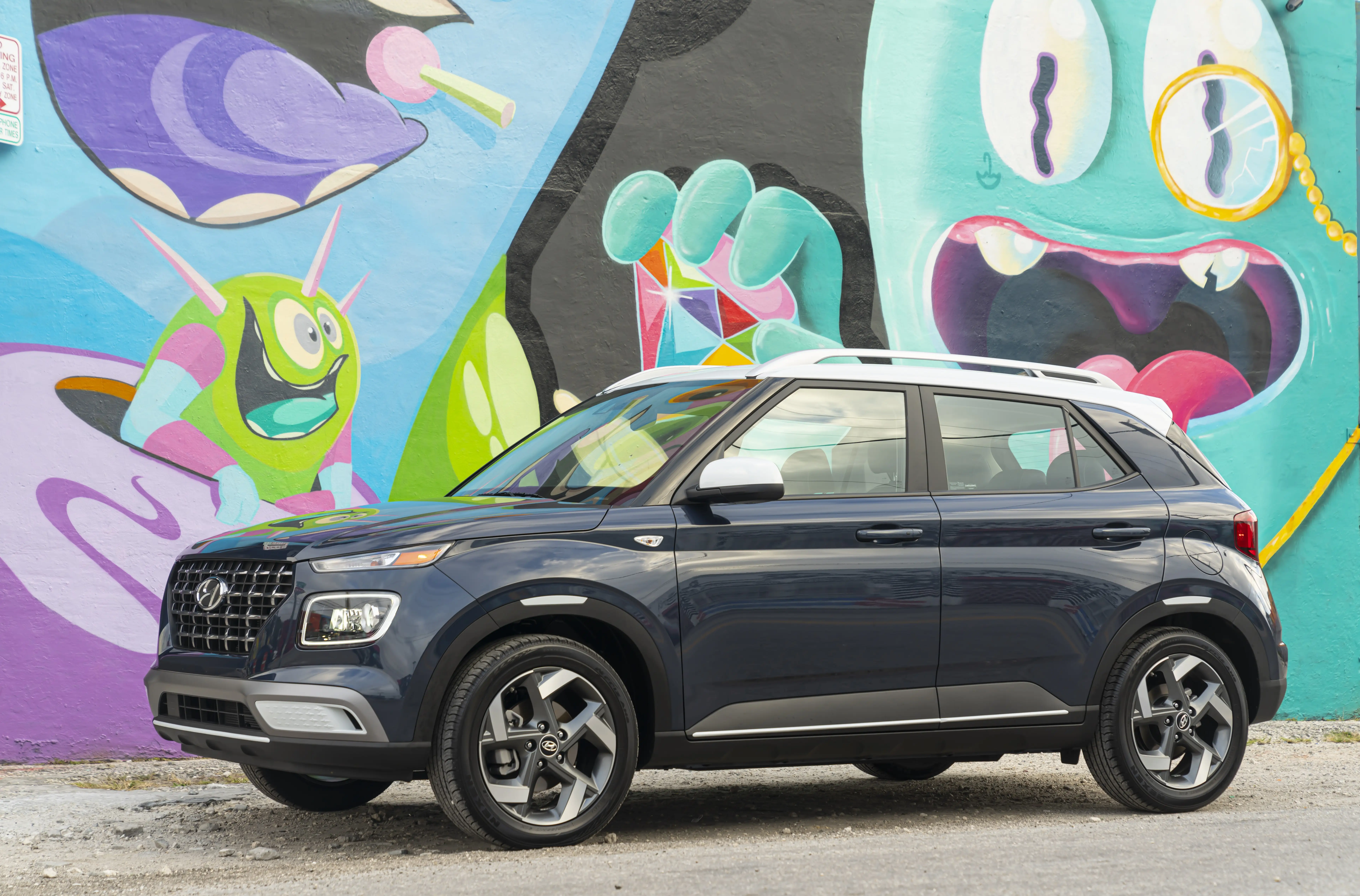 A dark blue Hyundai Venue with a white roofline is parked in front of a colorful mural.