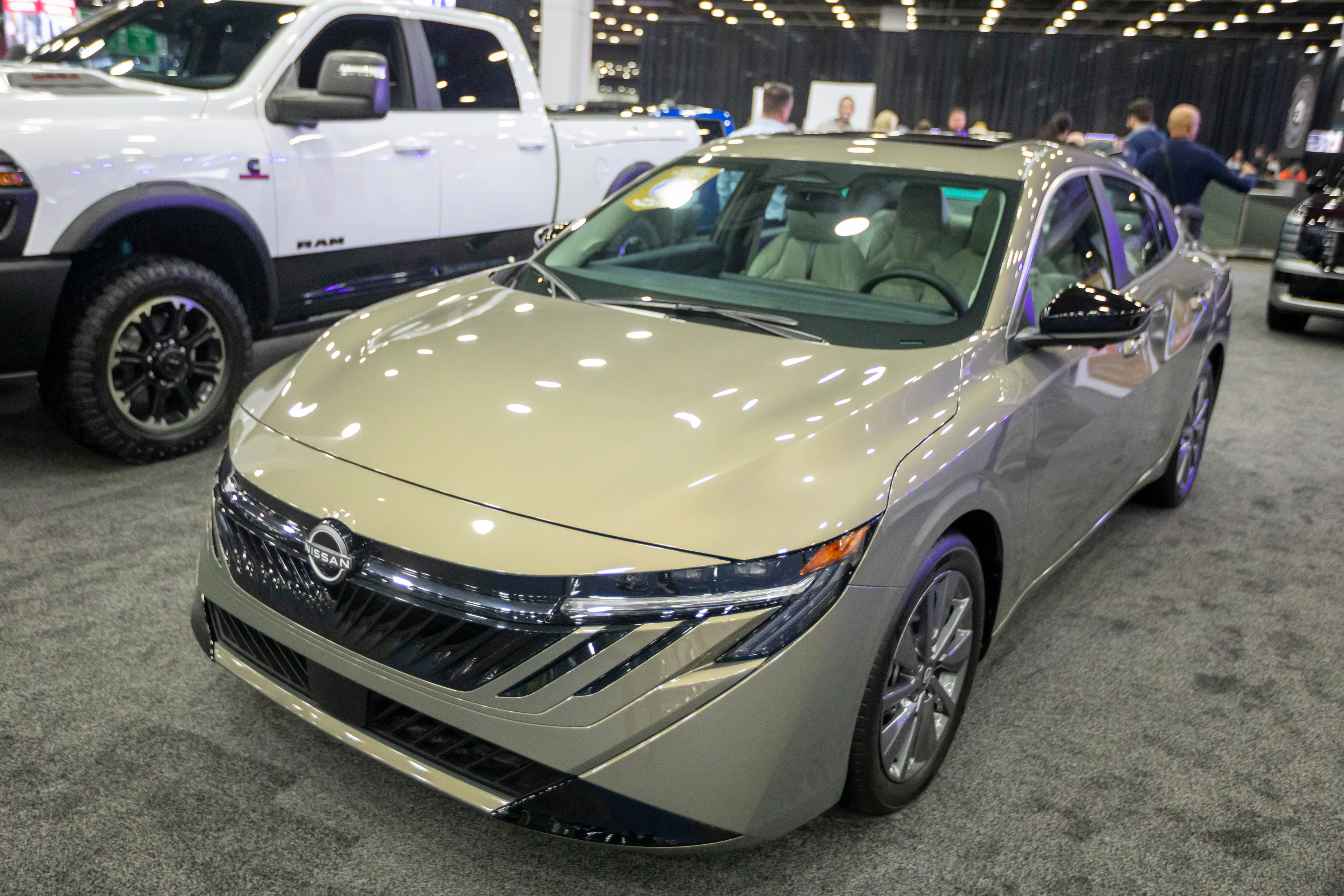 A beige Nissan Sentra sedan is parked on a carpeted floor at the Detroit Auto Show.