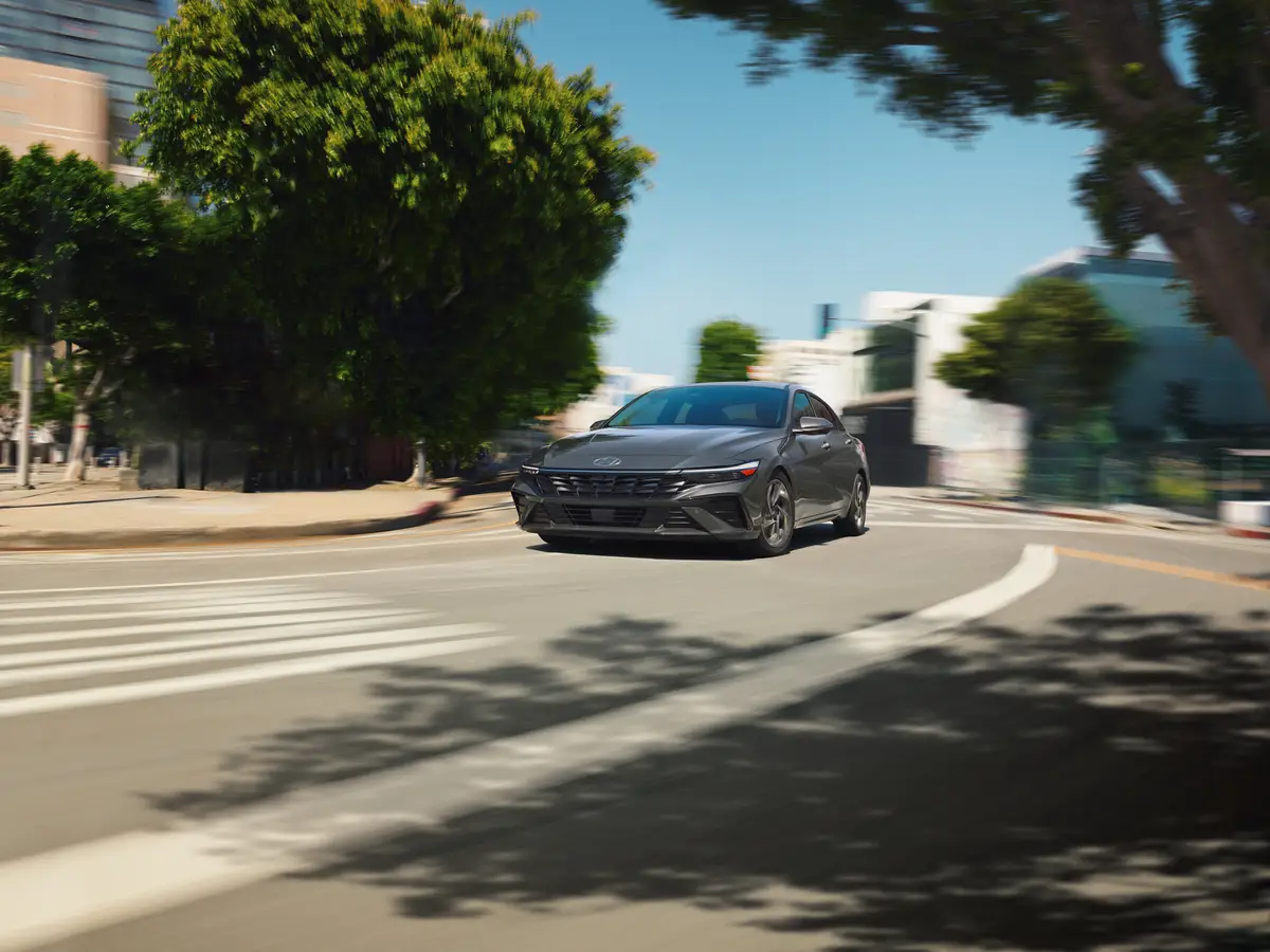 A gray Hyundai Elantra takes a turn on a tree-lined street.