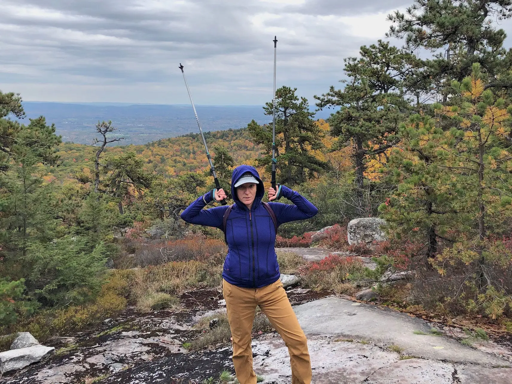Lindsey hikes in fall foliage while holding hiking poles over her head.