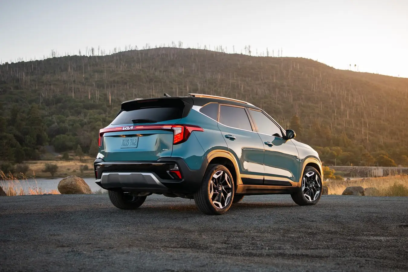 A turquoise Kia Seltos sits on a patch of gravel at dusk.