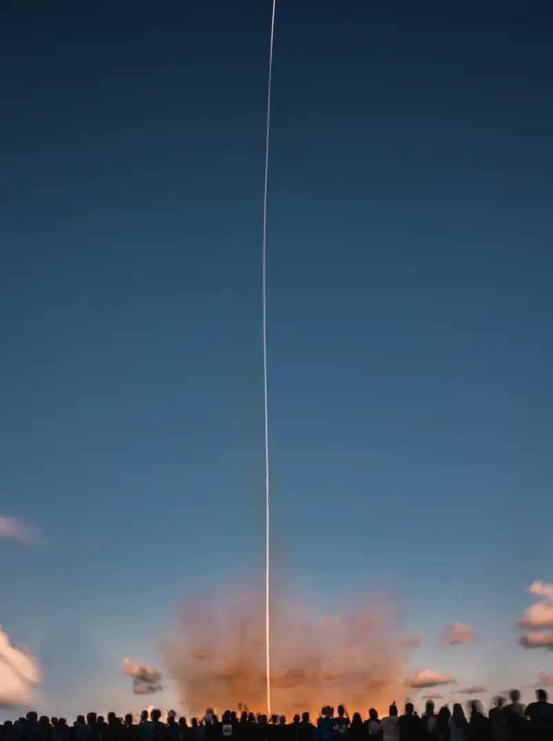 A line of onlookers watches as a SpaceX rocket streaks into a clear sky.